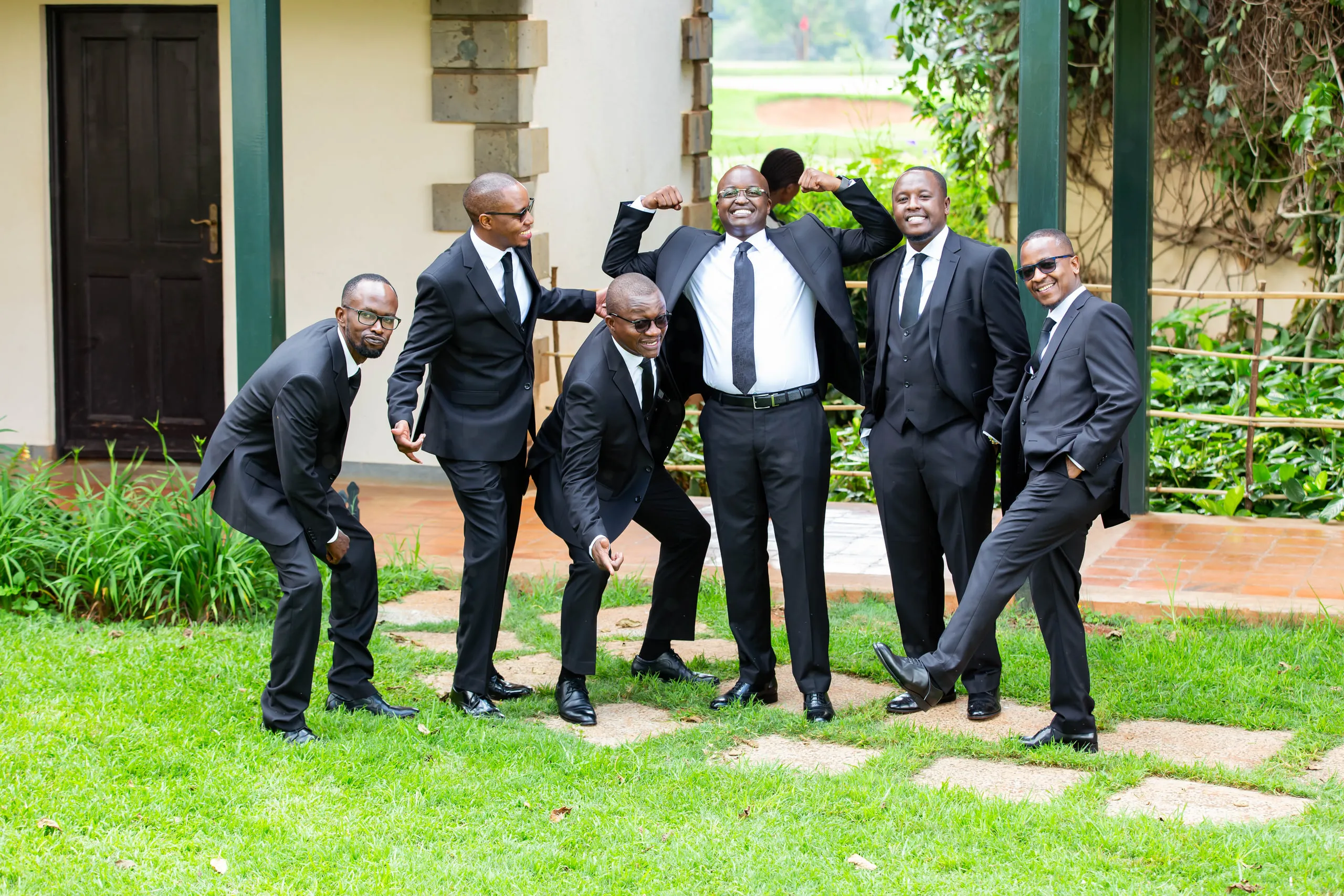 Groom and groomsmen in black suits clowning on a lawn
