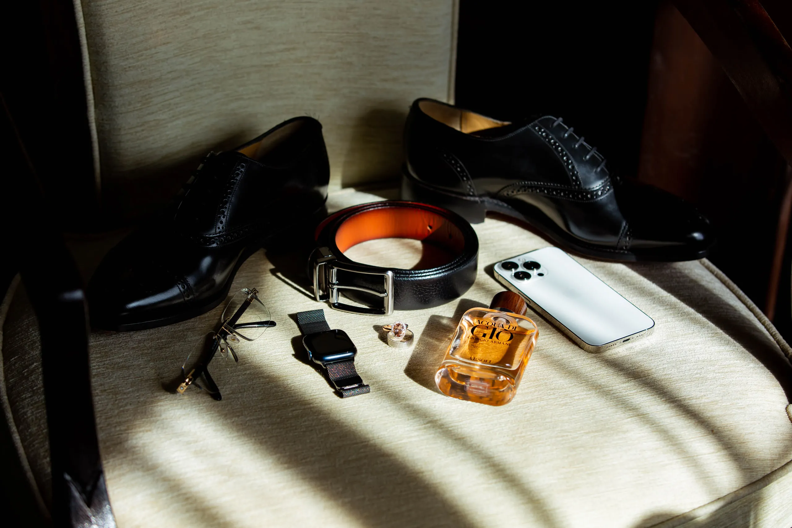 The groom's shoes, belt, cologne and phone laid out on a chair