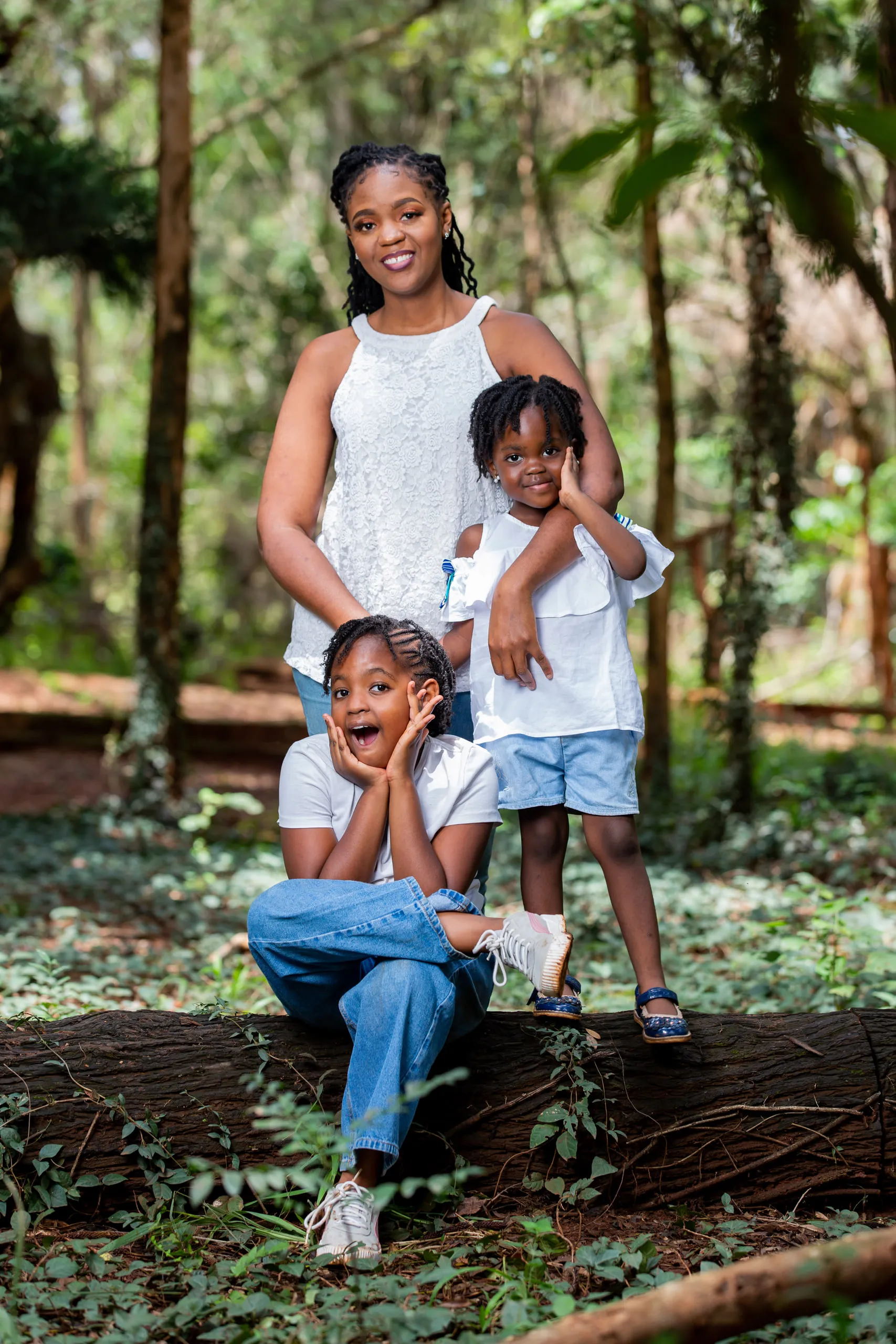 Mother standing in the forest with two children, one sitting on a log and one beside her
