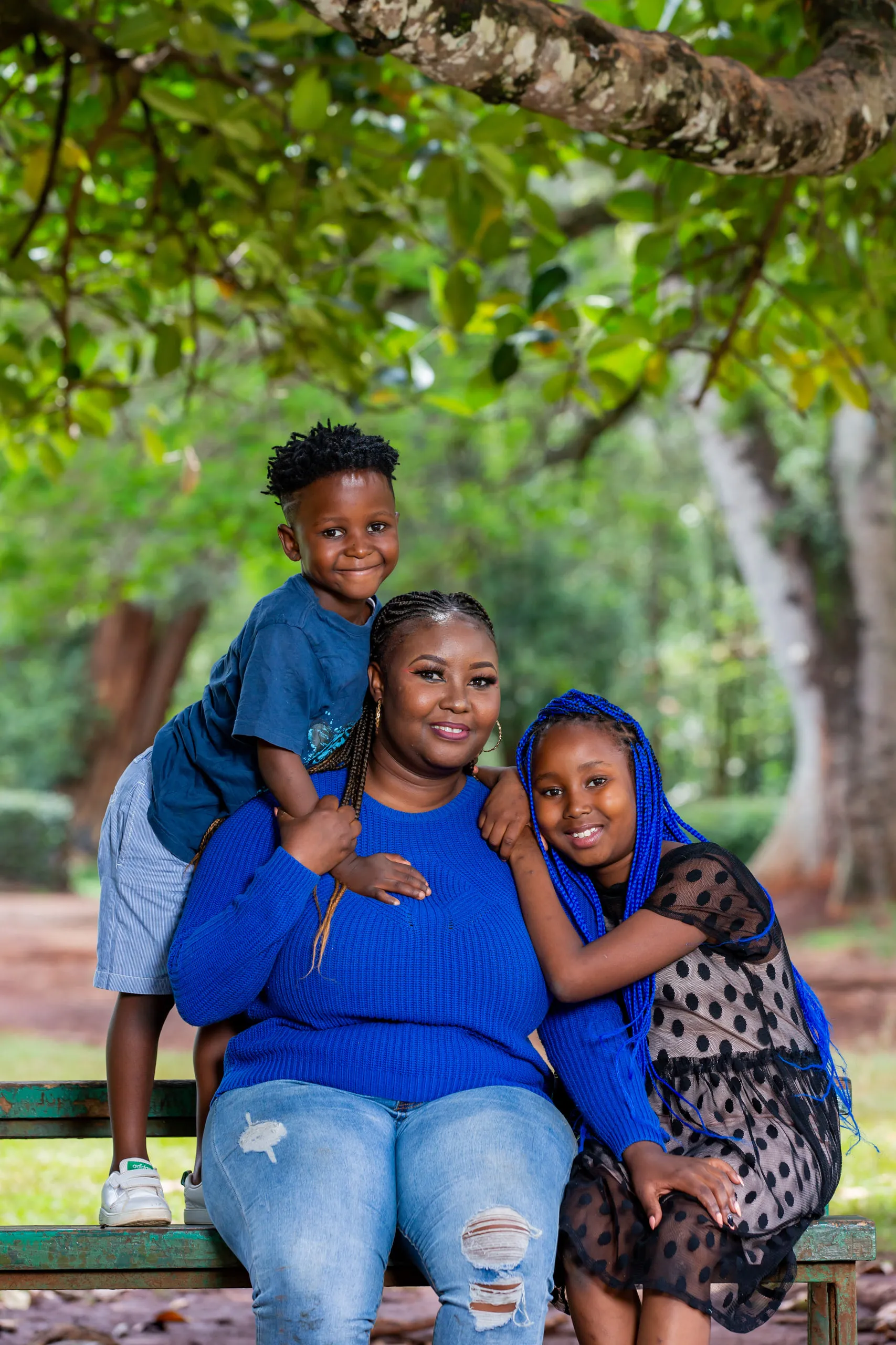 Mother on a park bench with a boy leaning on her shoulder and a girl in a polka-dot dress beside her