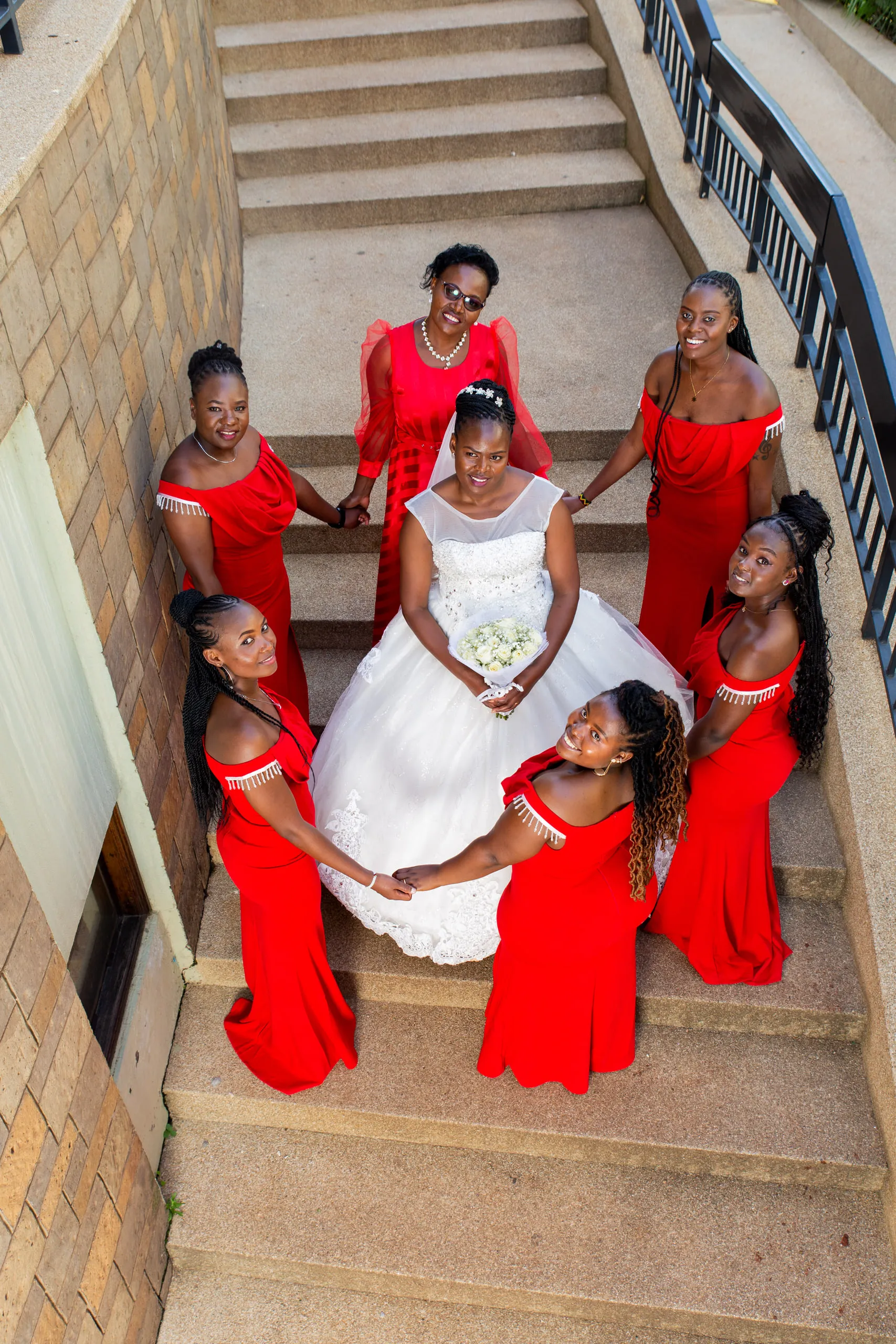 Bride surrounded by bridesmaids in red on a curved staircase, seen from above