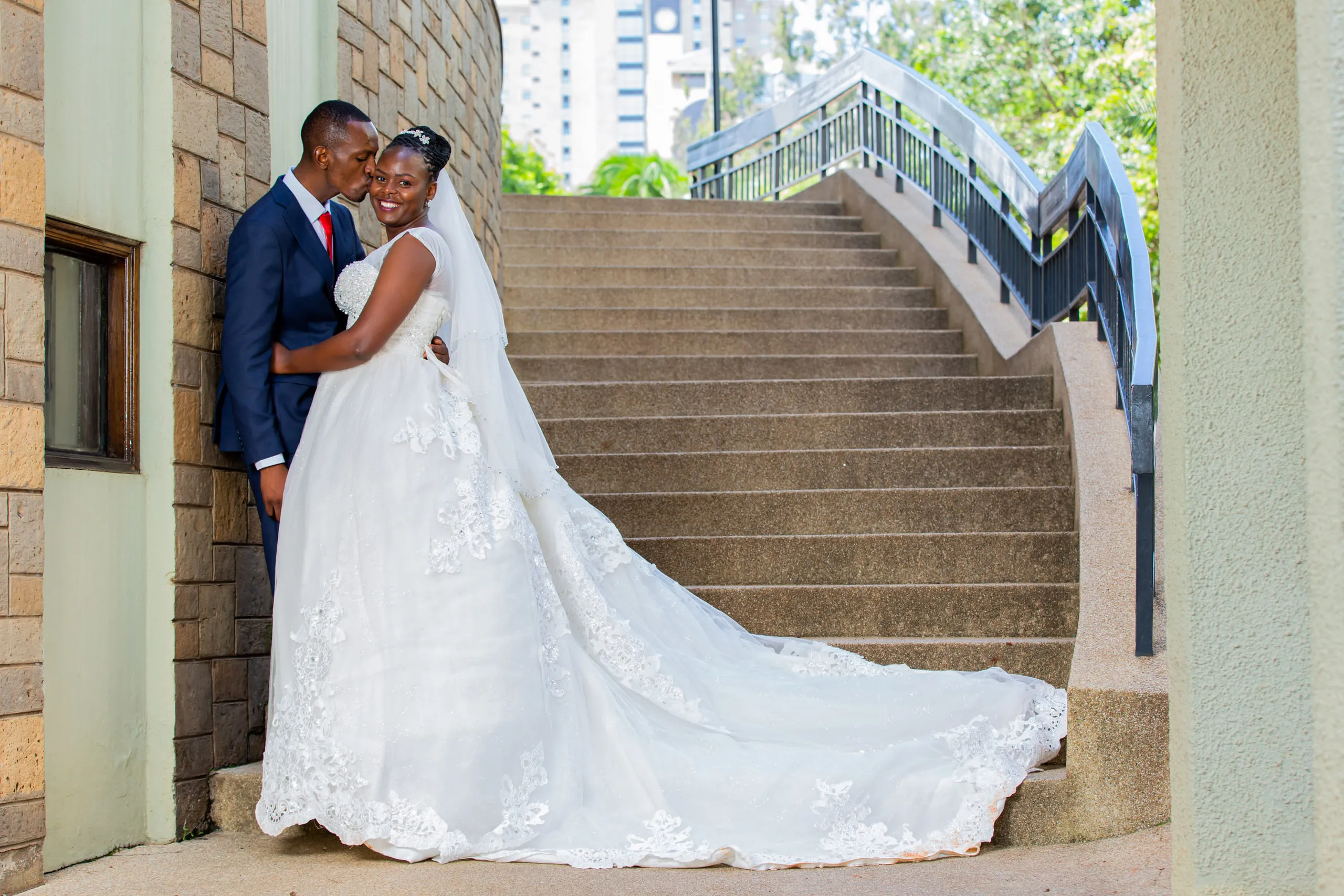 Bride and groom embracing at the foot of a stone staircase, her train spread out