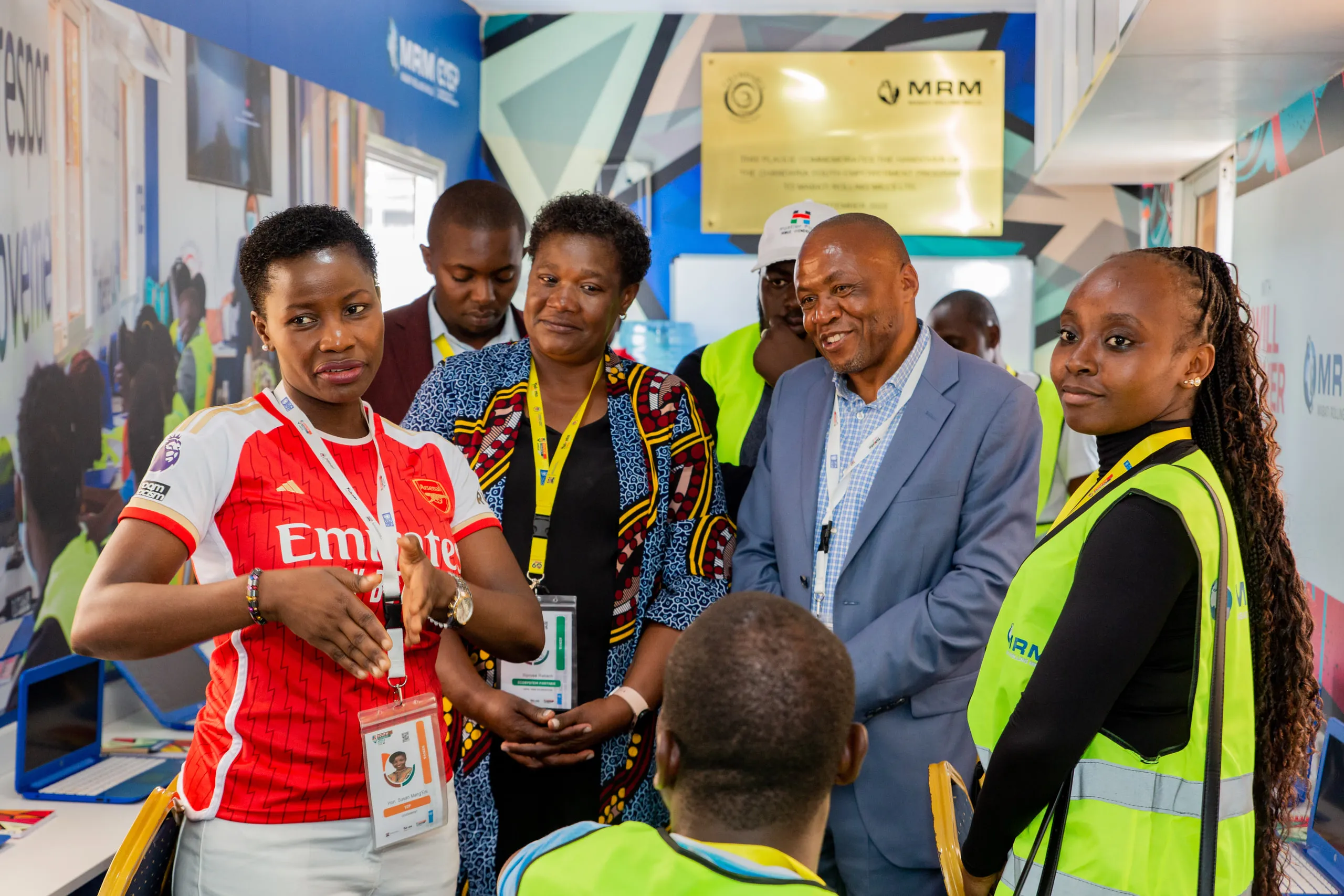 Group in conversation inside a branded container classroom, a woman in a red football shirt speaking