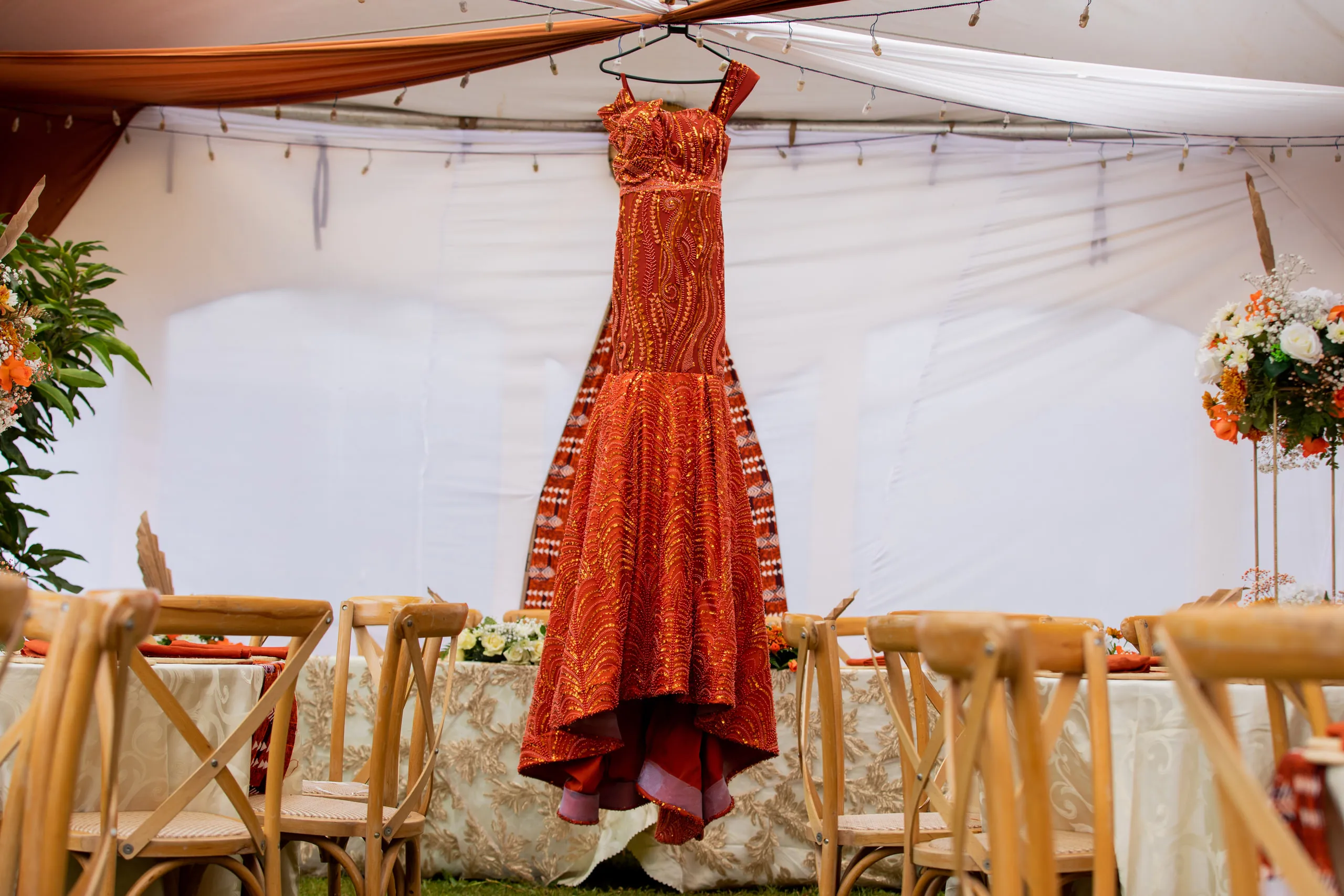 Orange gown hanging in a white tent above rows of chairs
