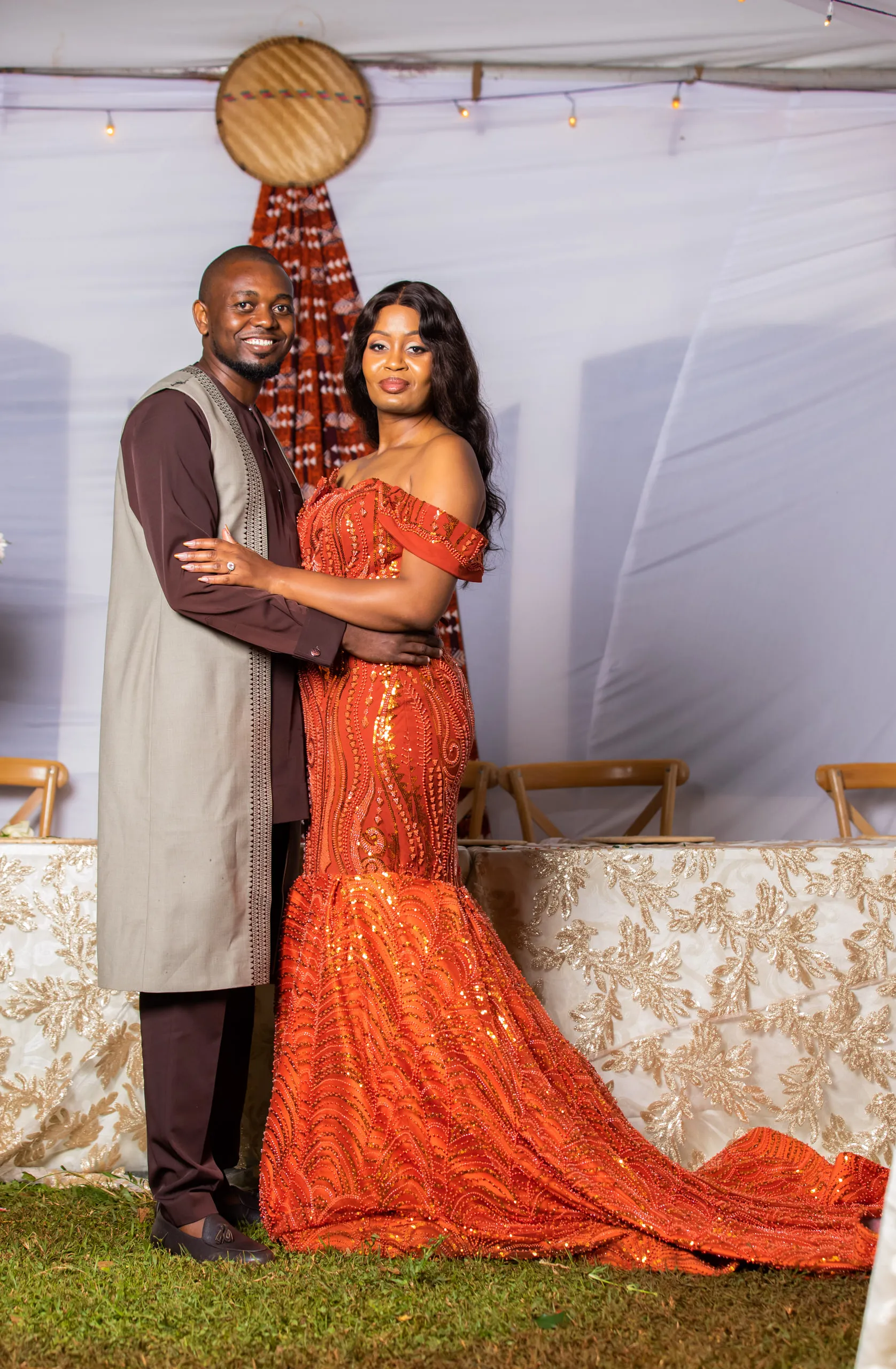 Couple under a tent, she in a long orange gown with a train, he in a grey tunic