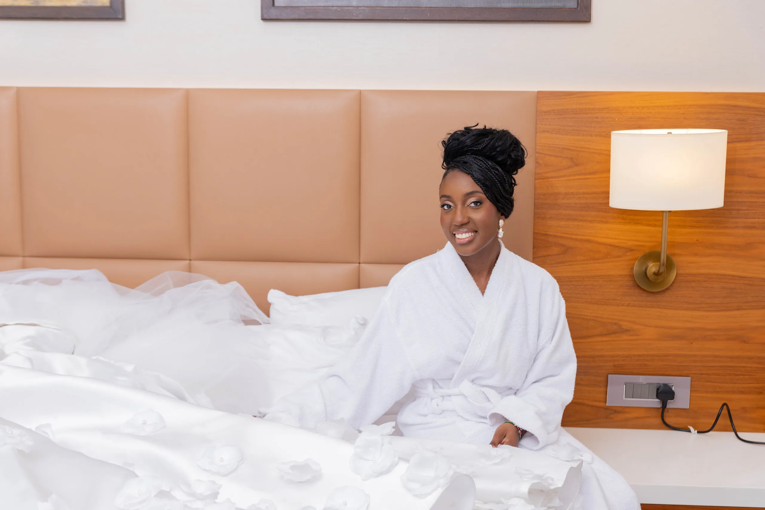 Bride in a white robe laughing on the bed during the morning preparations