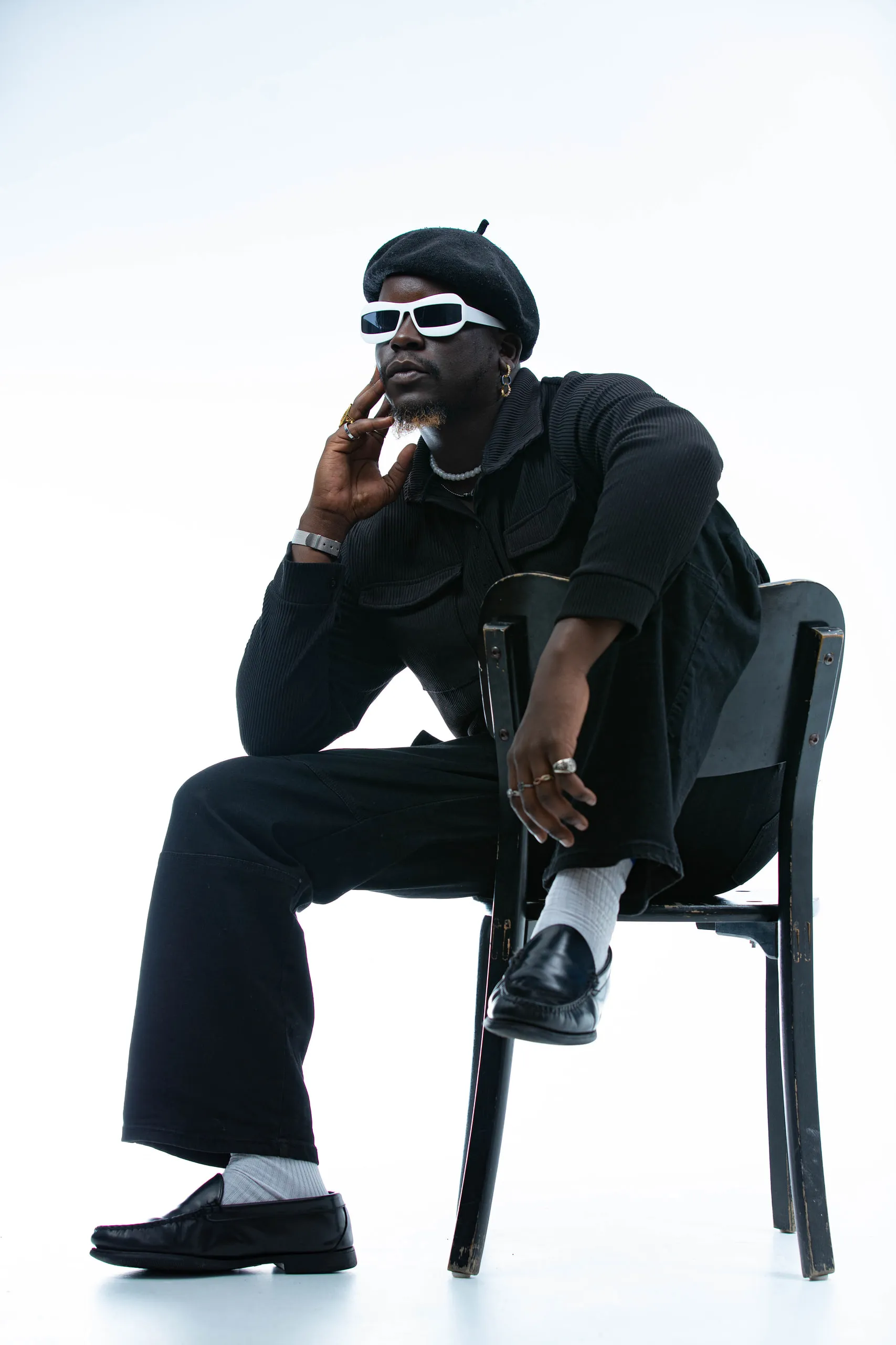Man in a beret and white sunglasses resting his chin on his hand while seated on a black chair