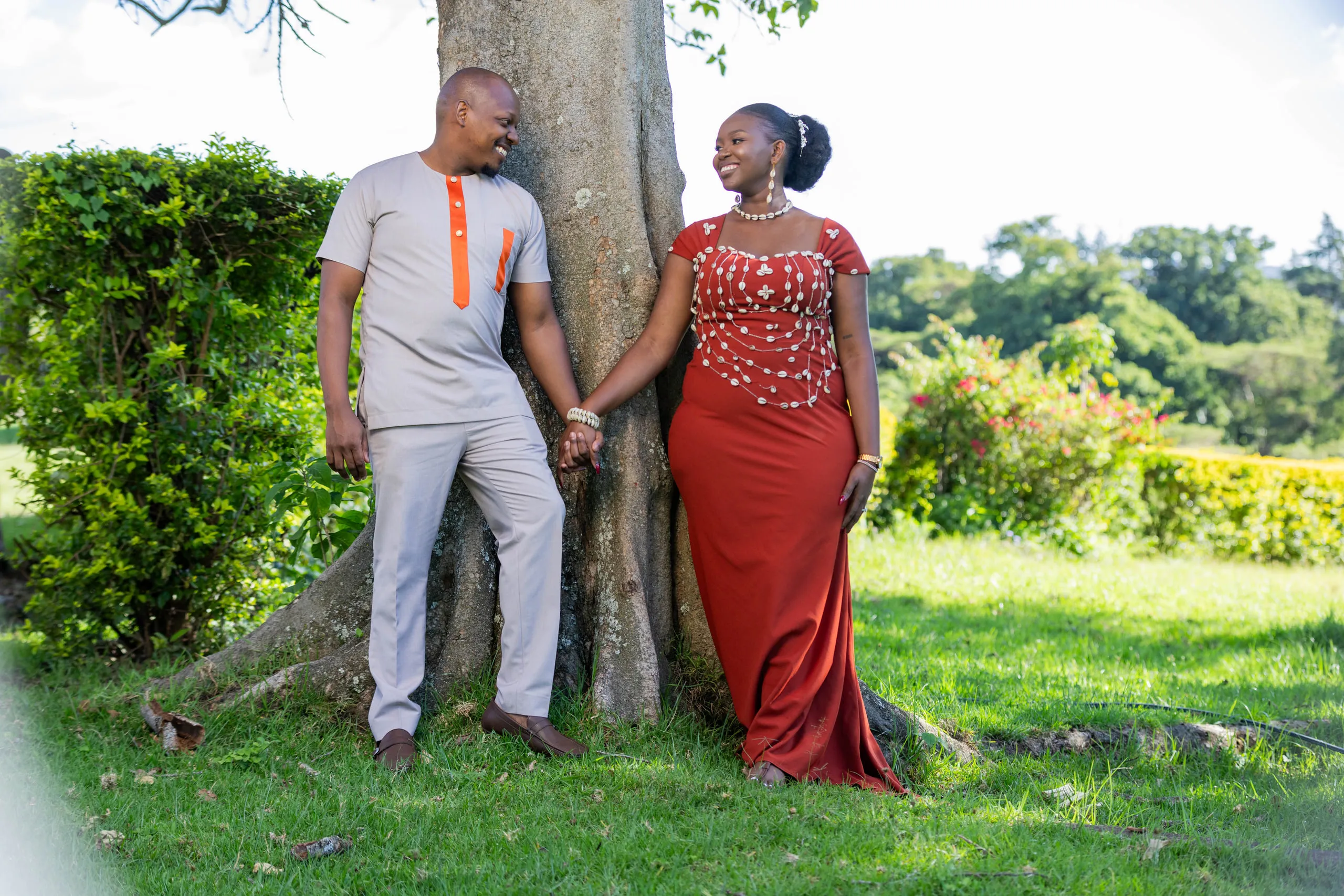 Couple holding hands by a large tree, she in red, he in grey with orange trim