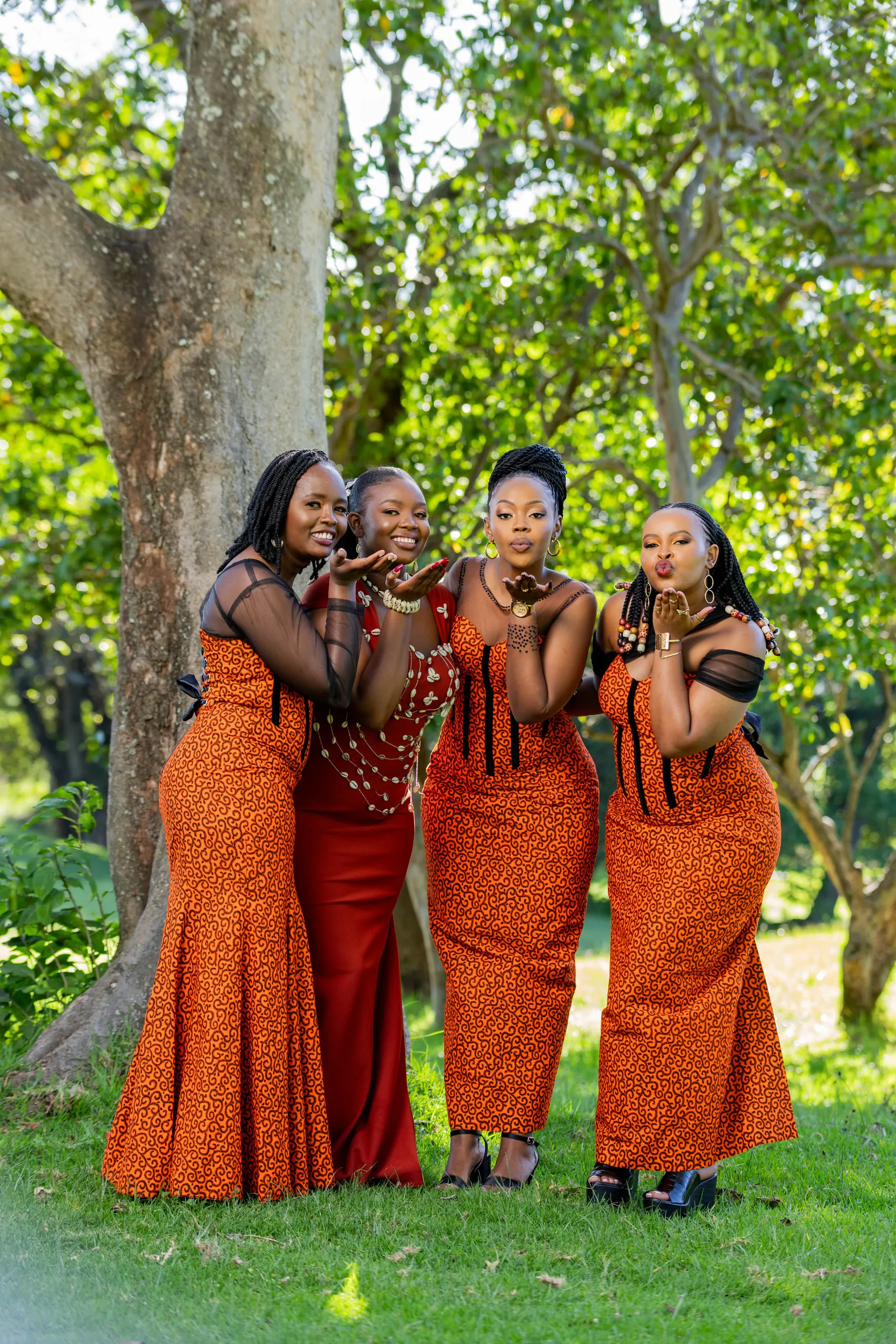 Four women in orange dresses blowing kisses under a tree