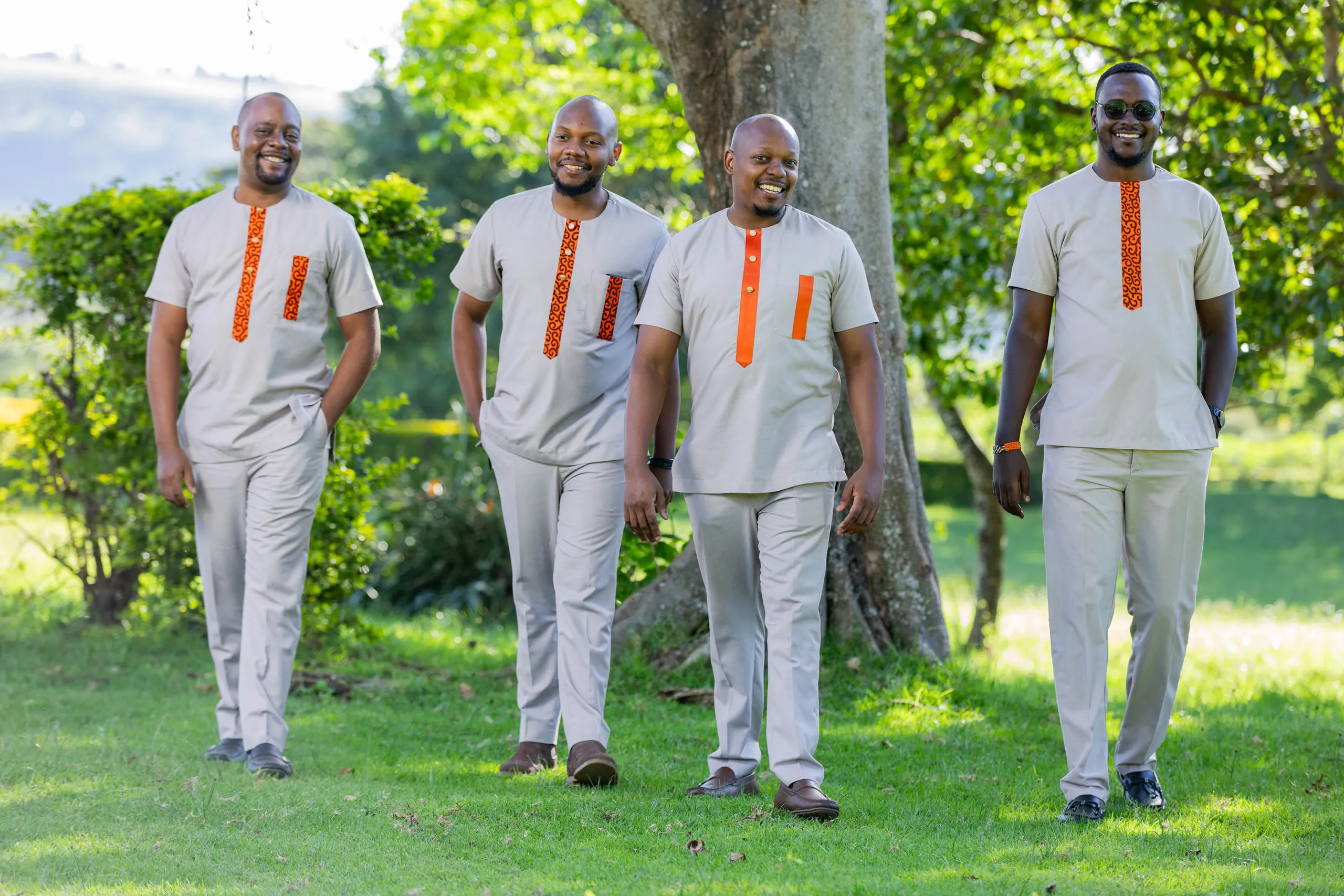 Four groomsmen in matching tunics walking across the grass