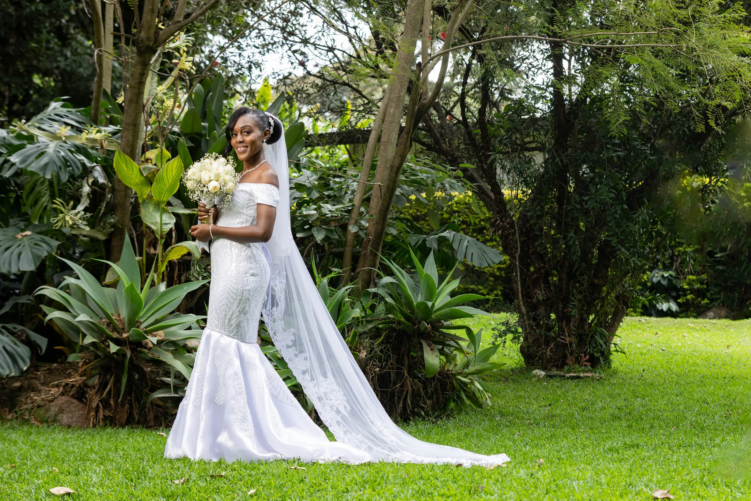Bride with a long veil holding her bouquet on a garden lawn