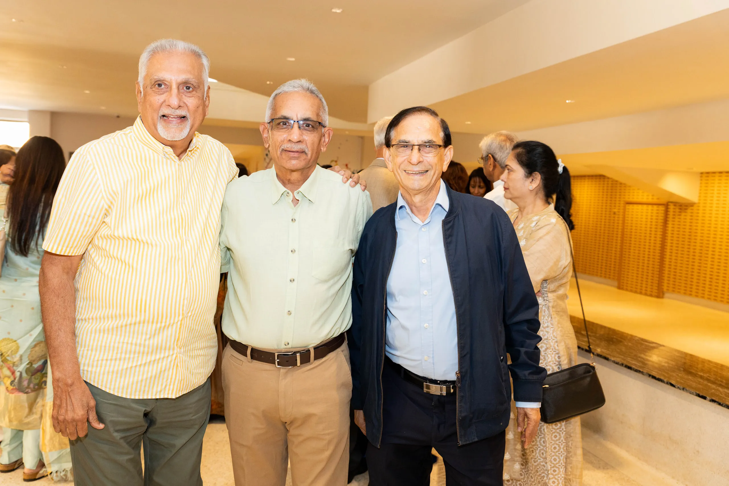 Three older men with their arms around each other in a temple hall