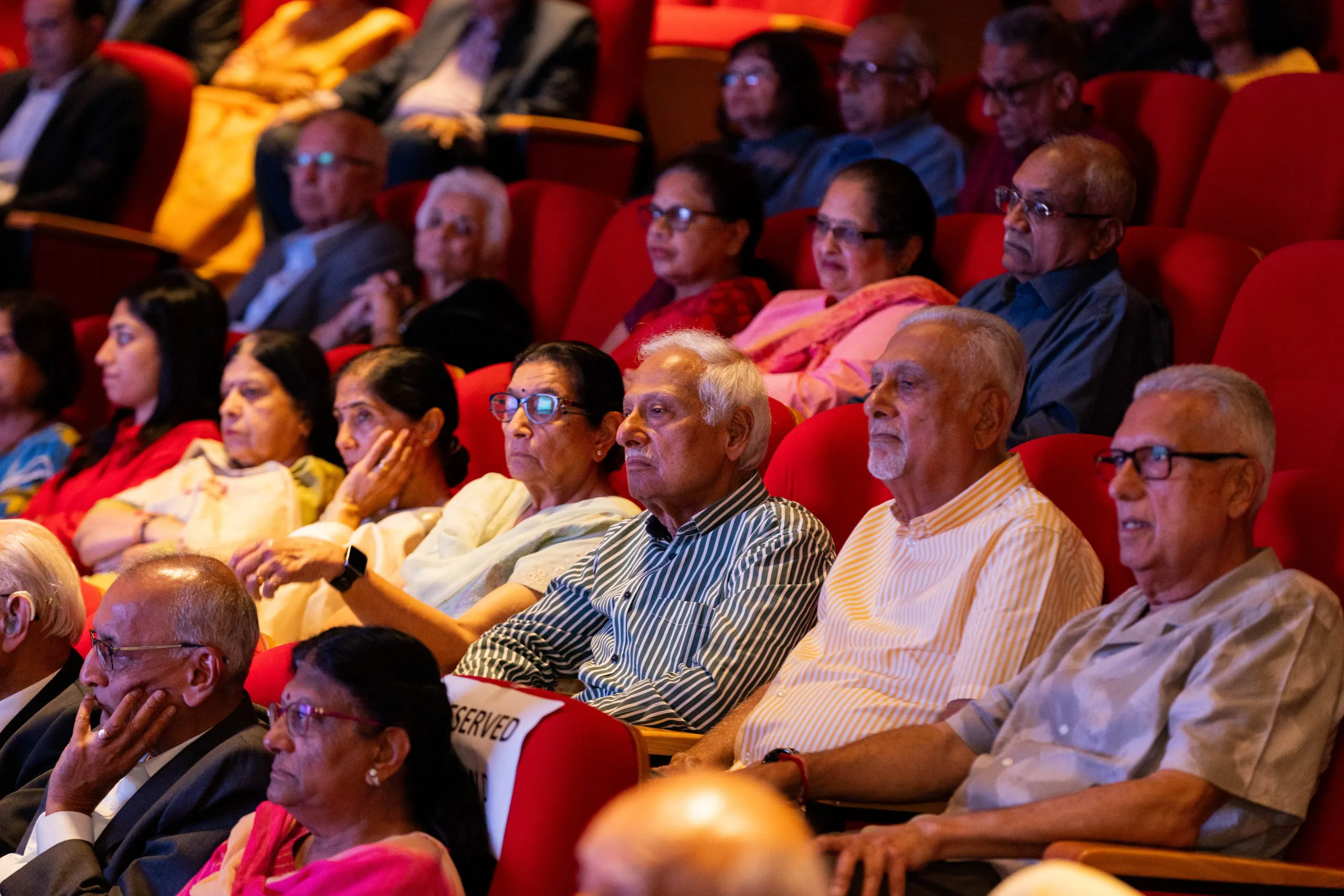 Older audience members in red theatre seats watching a talk