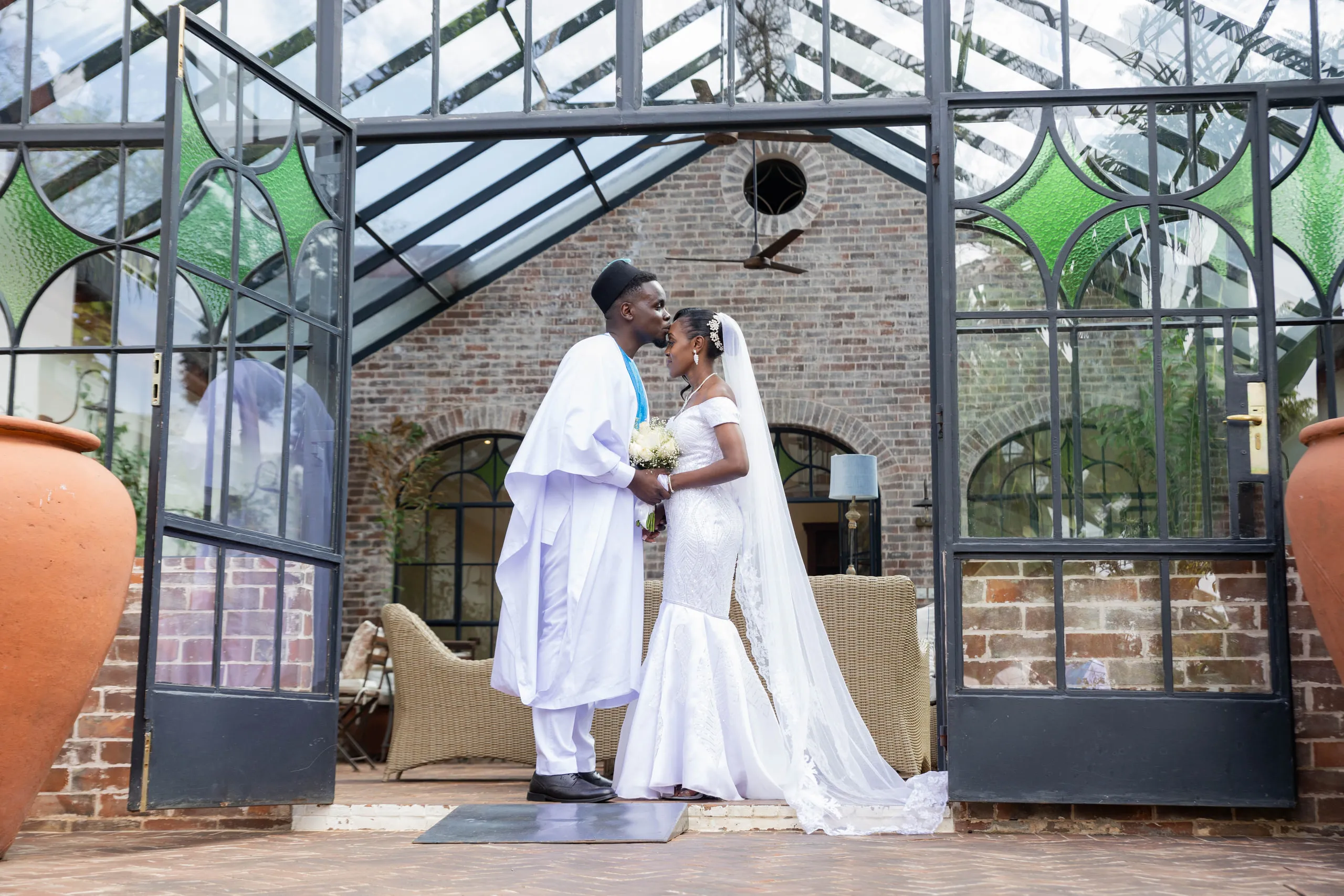 Bride and groom kissing in the doorway of a glasshouse