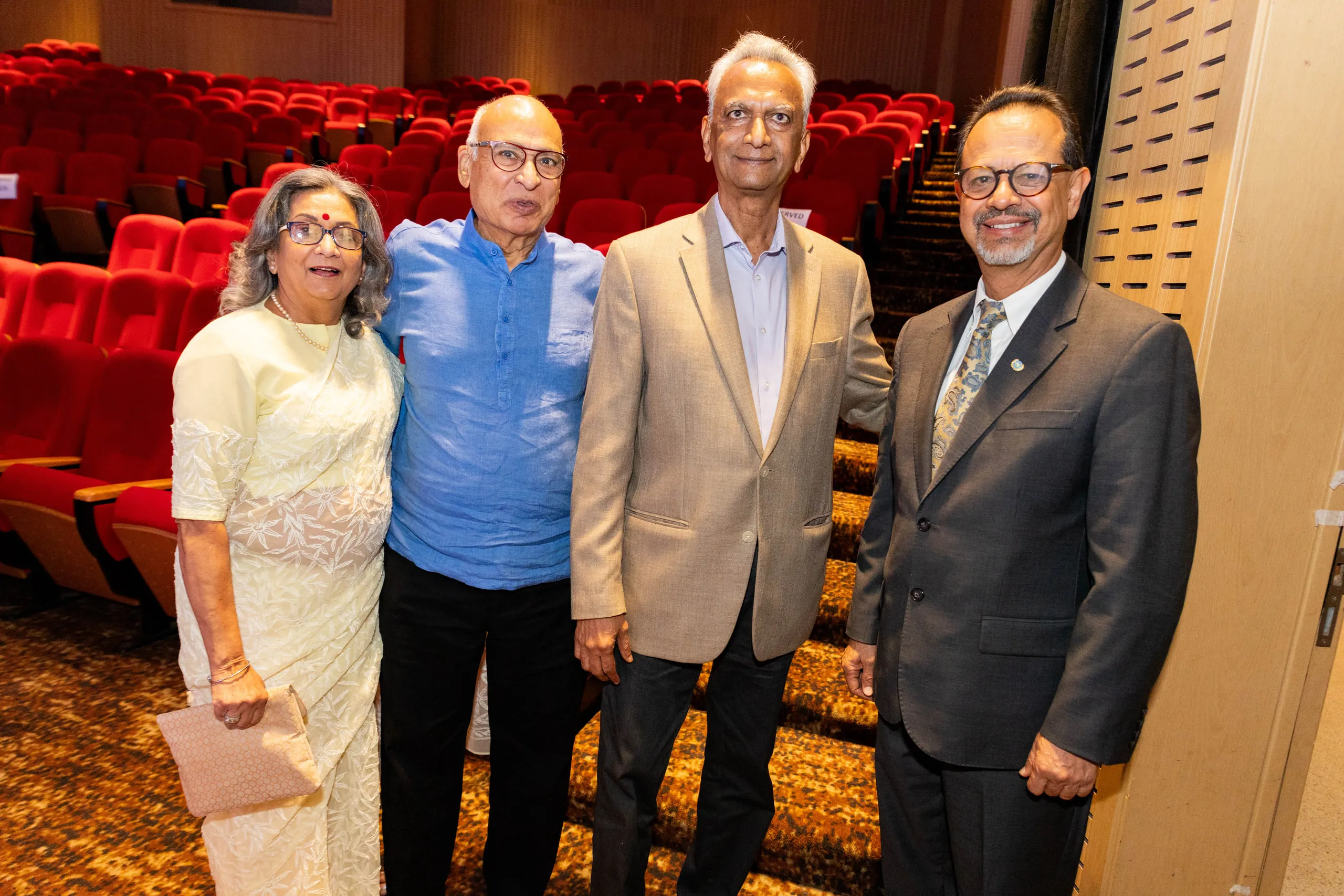 Four people in a row posing in front of rows of red theatre seats