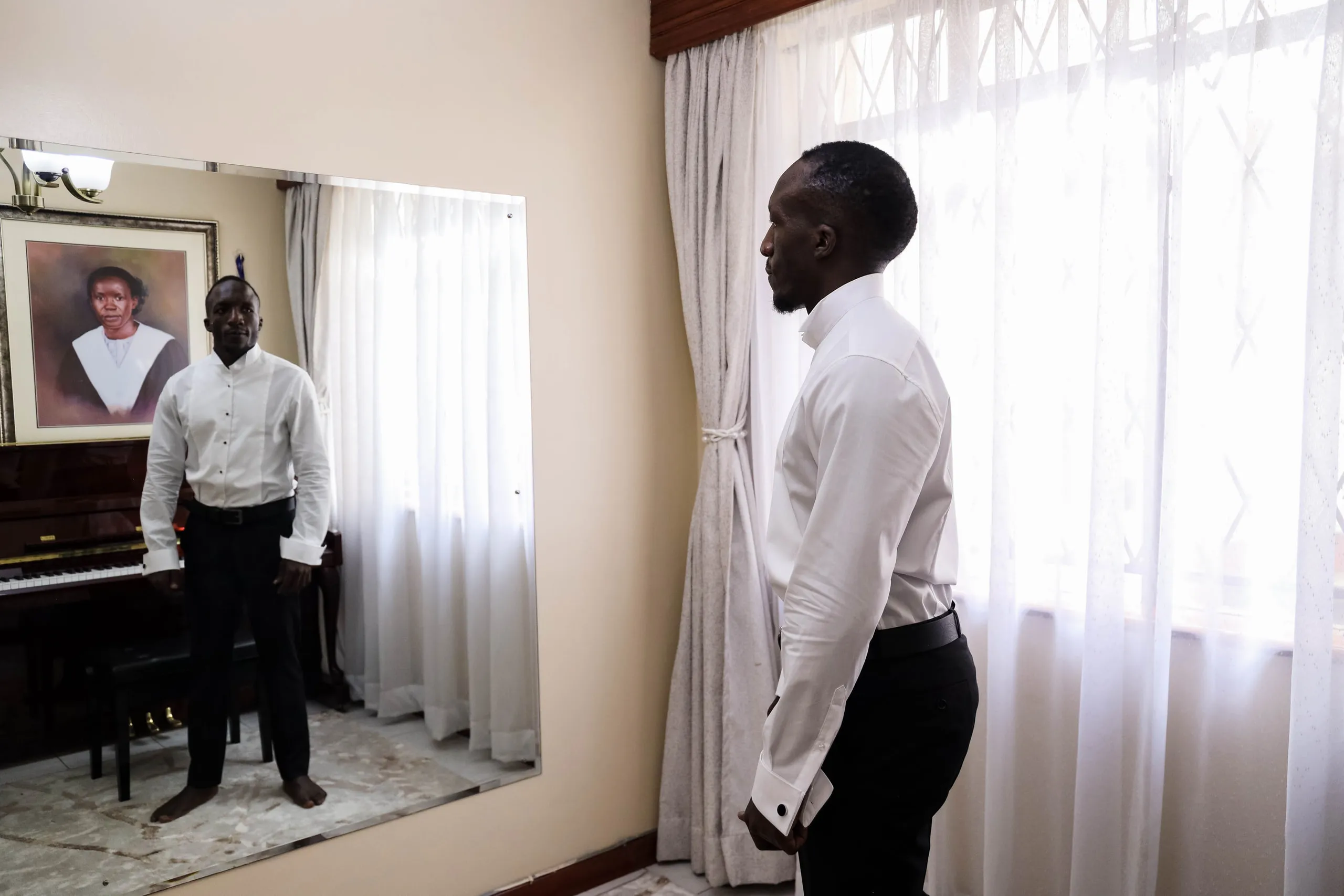 Groom by a bright window while a friend waits behind him