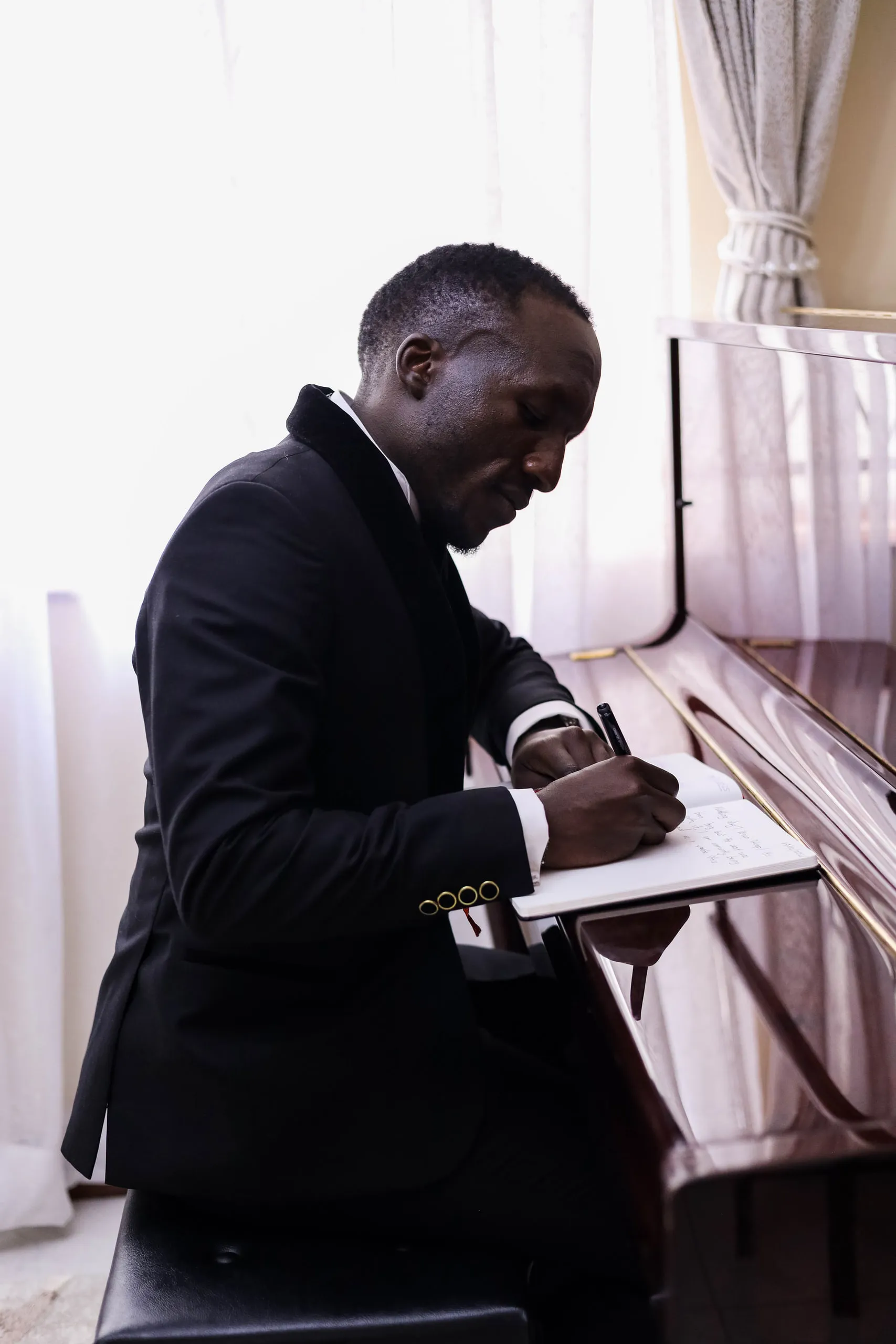 Groom in a tuxedo writing at a piano