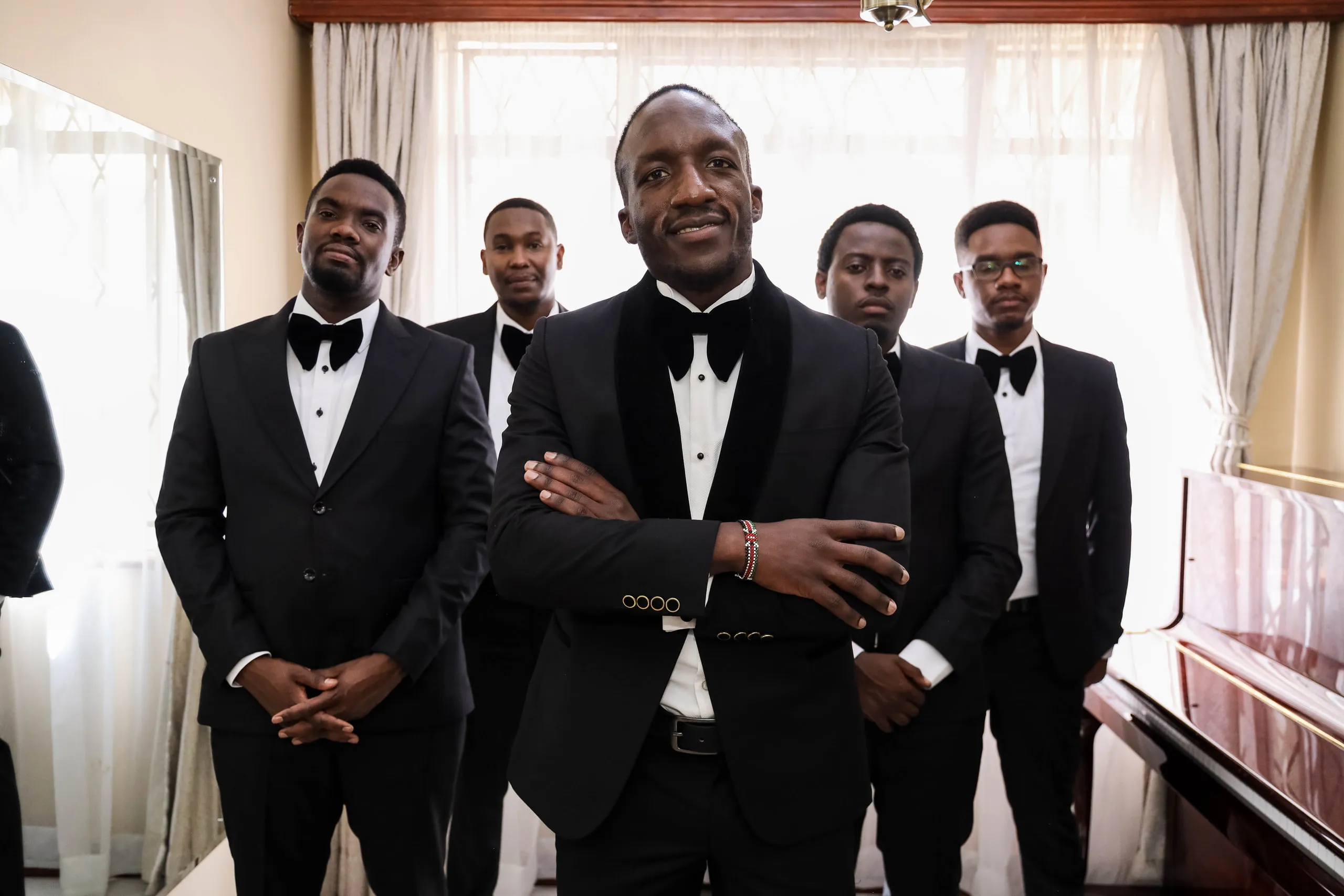 Groom and groomsmen in tuxedos by a tall window