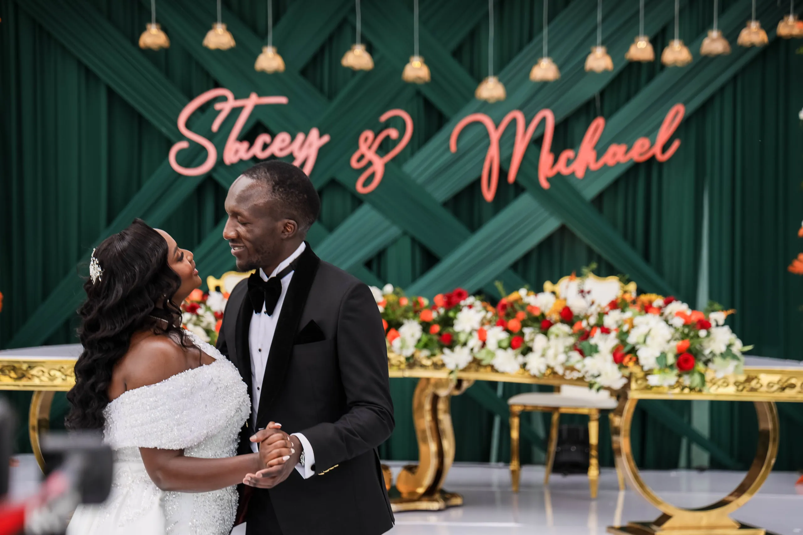 Bride and groom dancing in front of a green floral backdrop