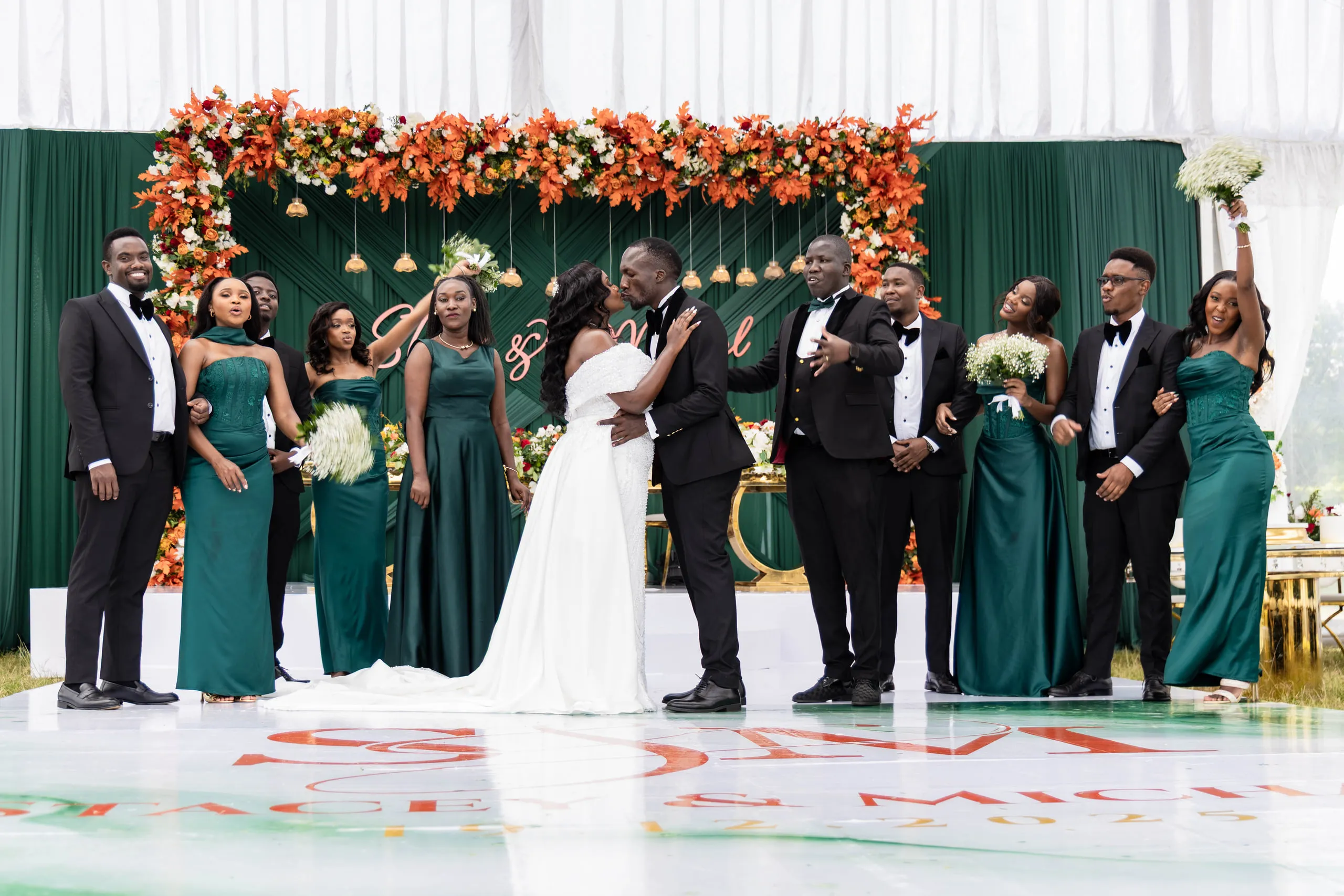 Bride and groom kissing with the wedding party in green behind them