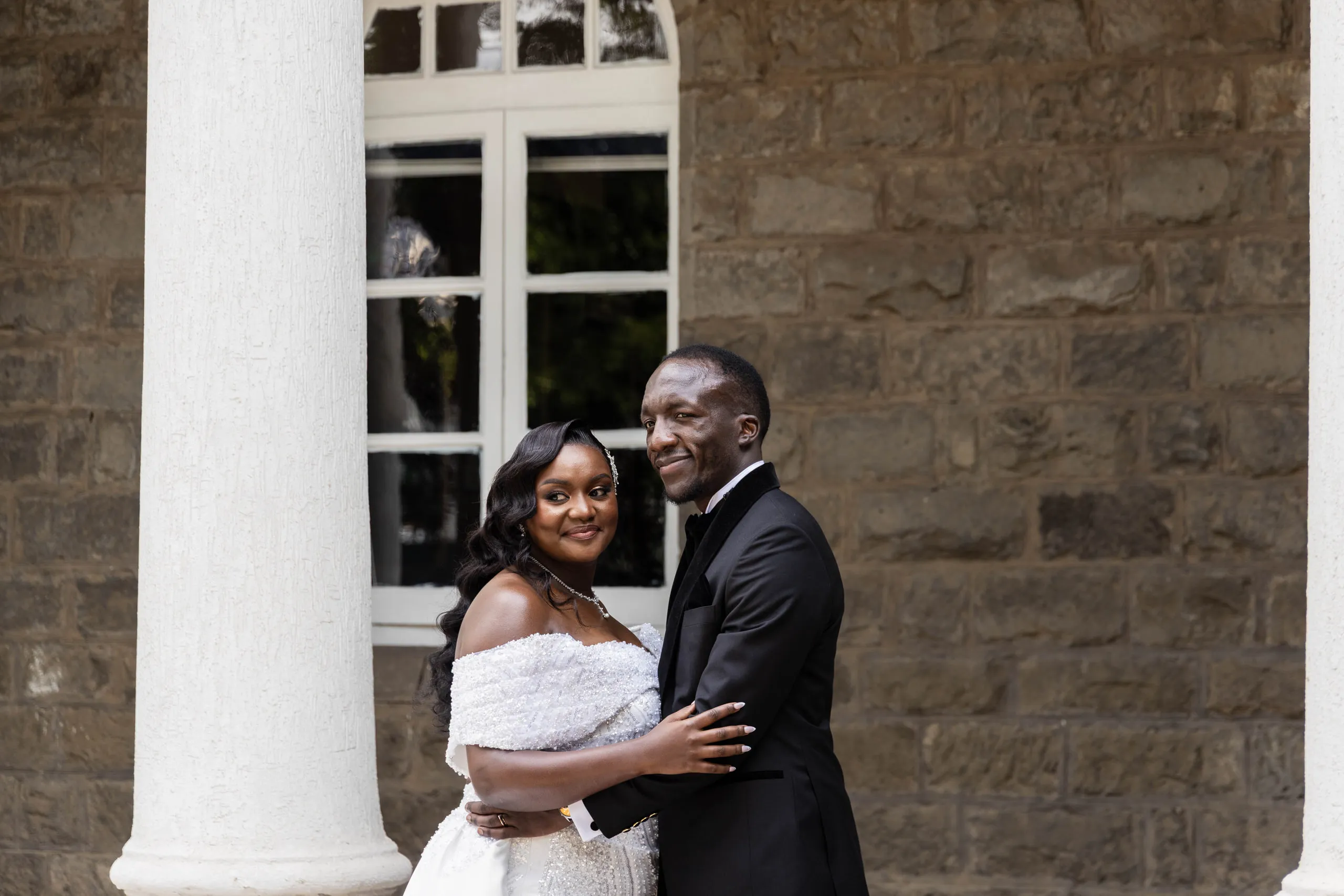 Bride and groom holding each other beside a stone wall