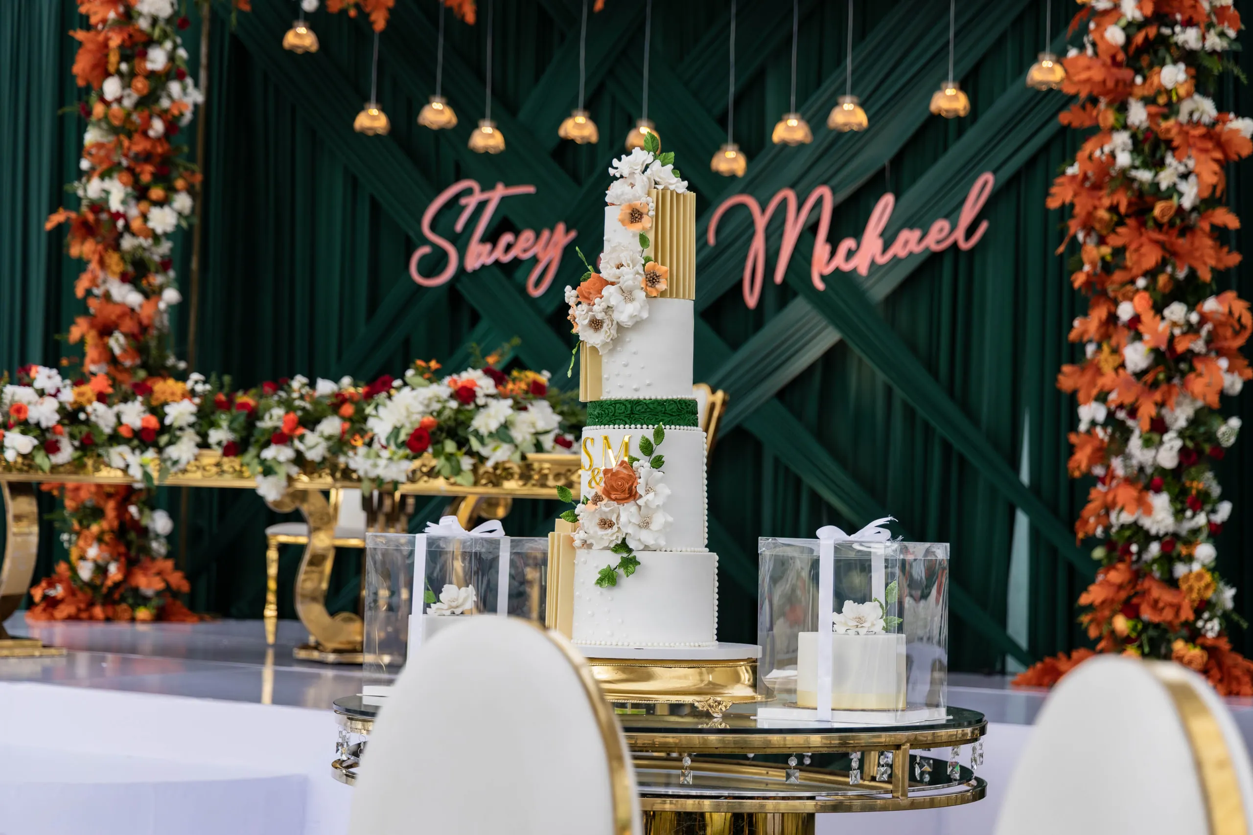 The wedding cake on a gold table in front of the floral backdrop