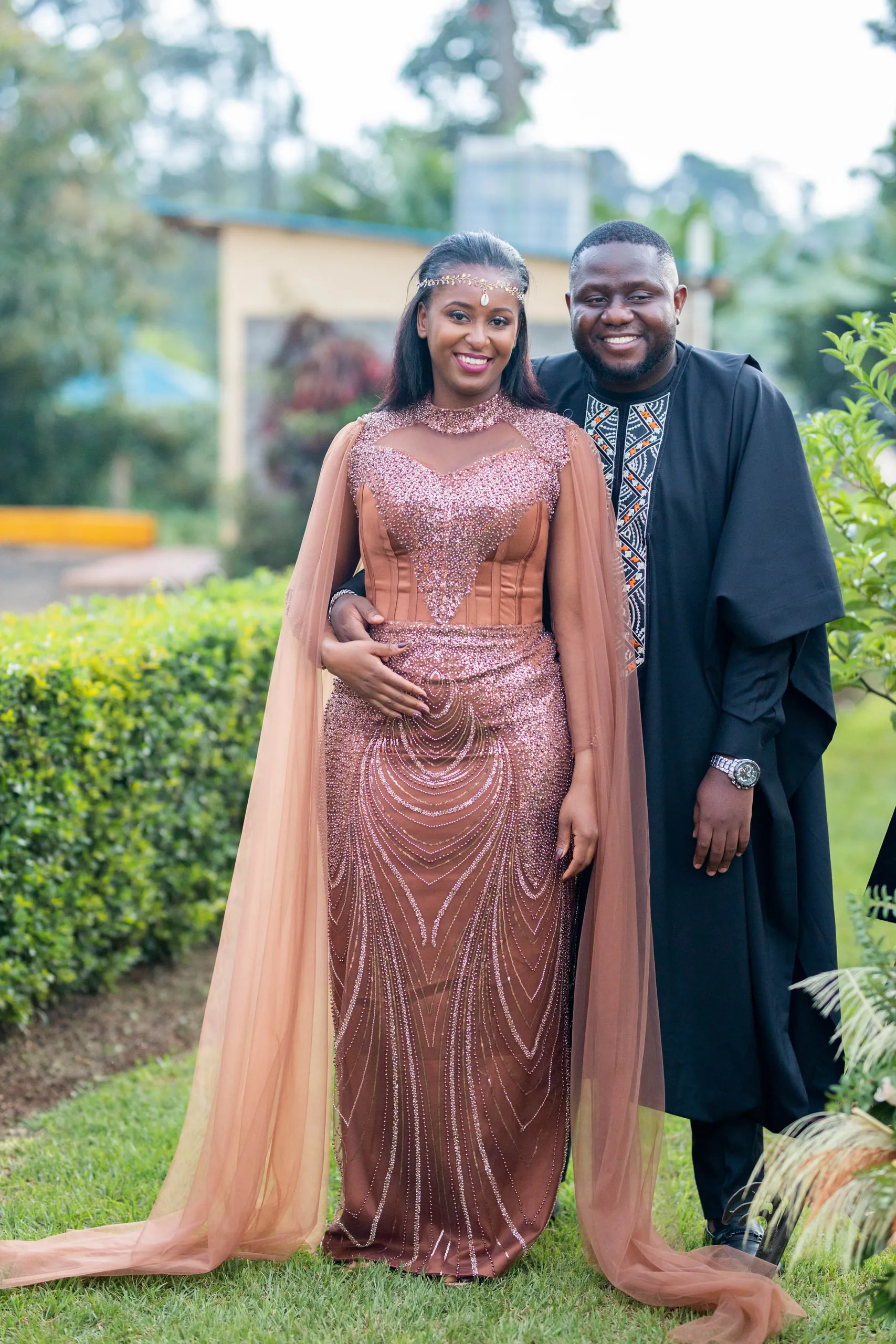 Couple on a lawn, she in a blush beaded gown with a long cape, he in a dark embroidered robe