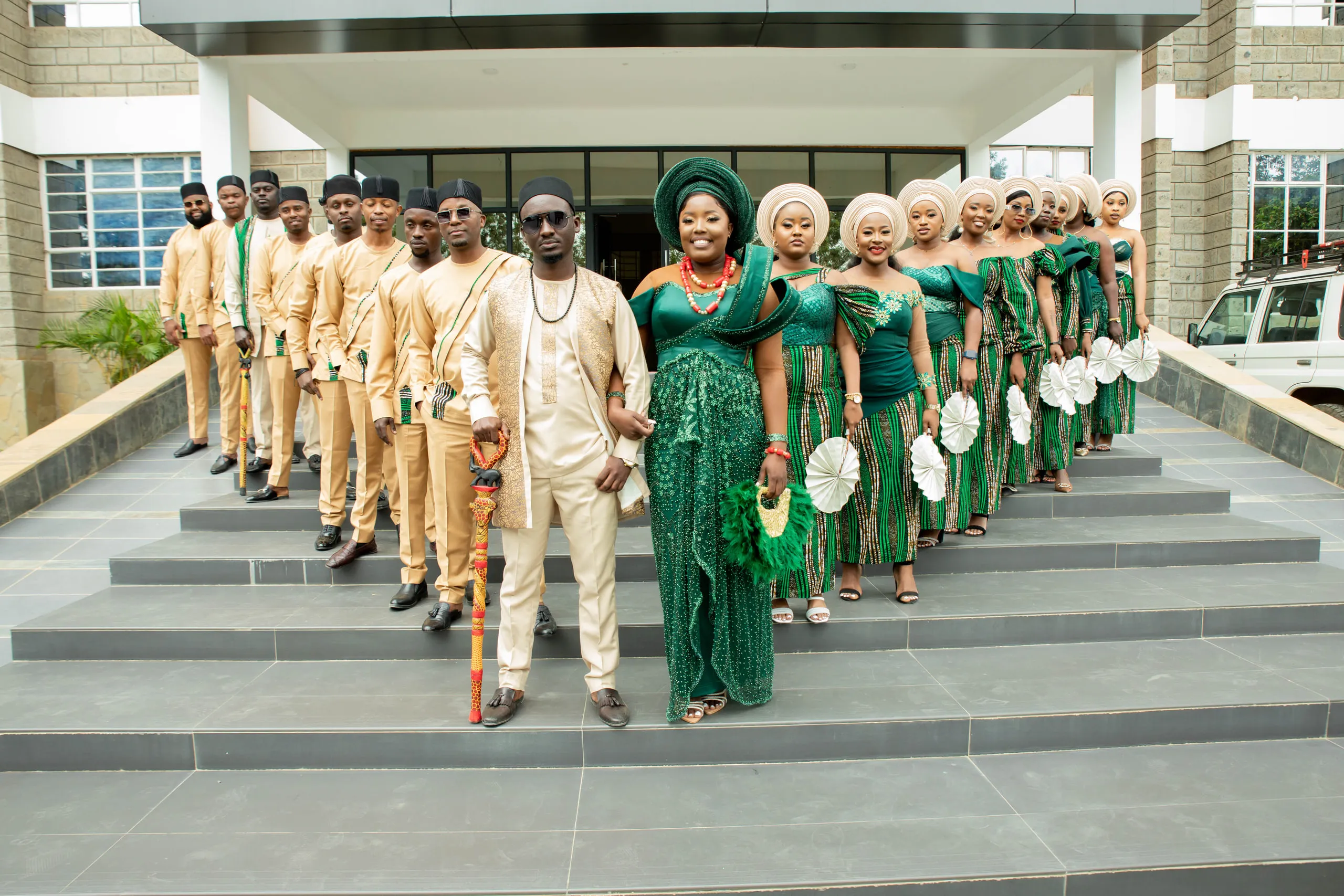 The whole wedding party in green and gold on the steps of a building