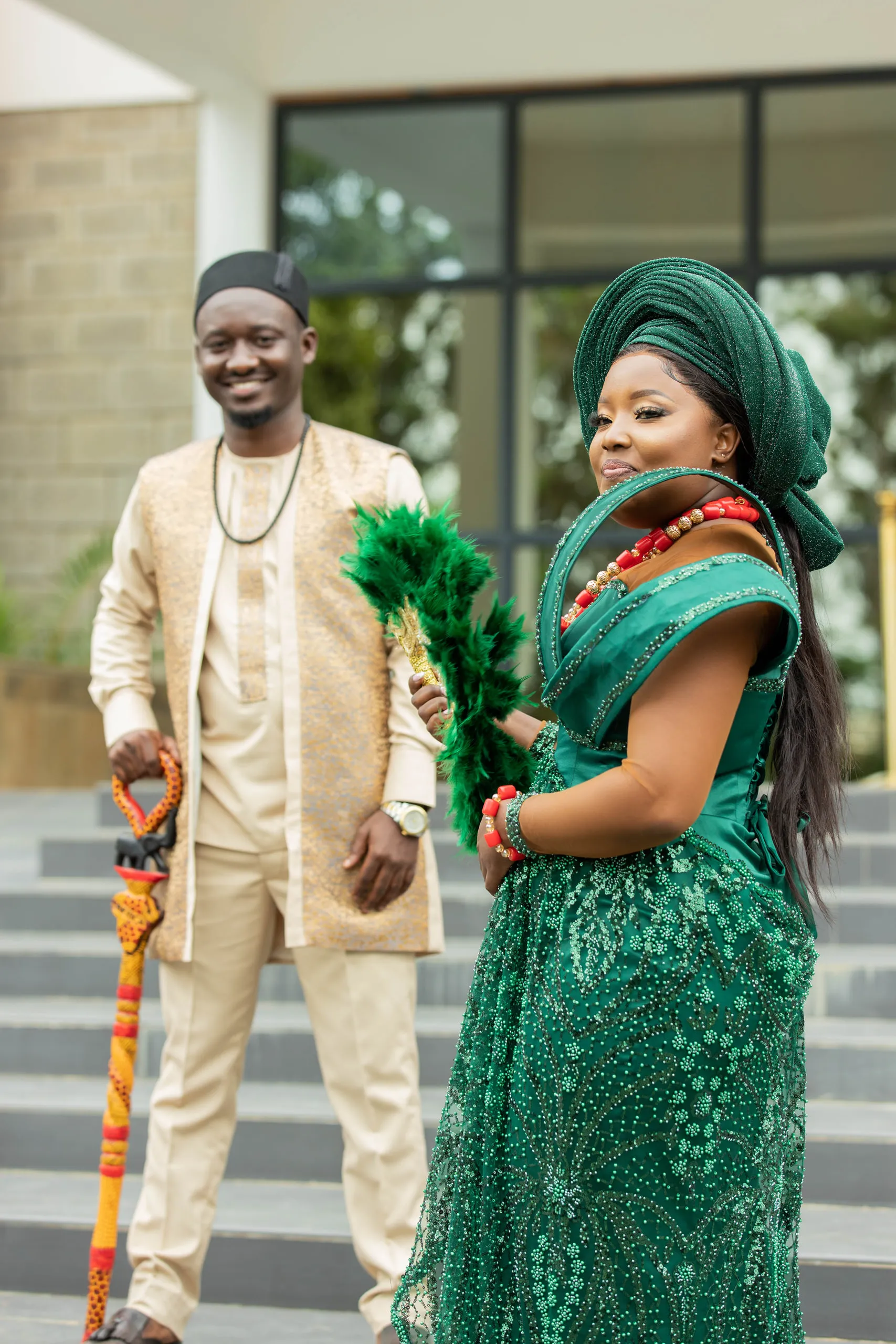 Couple in green and cream on the steps, she with a feather fan, he with a carved walking stick