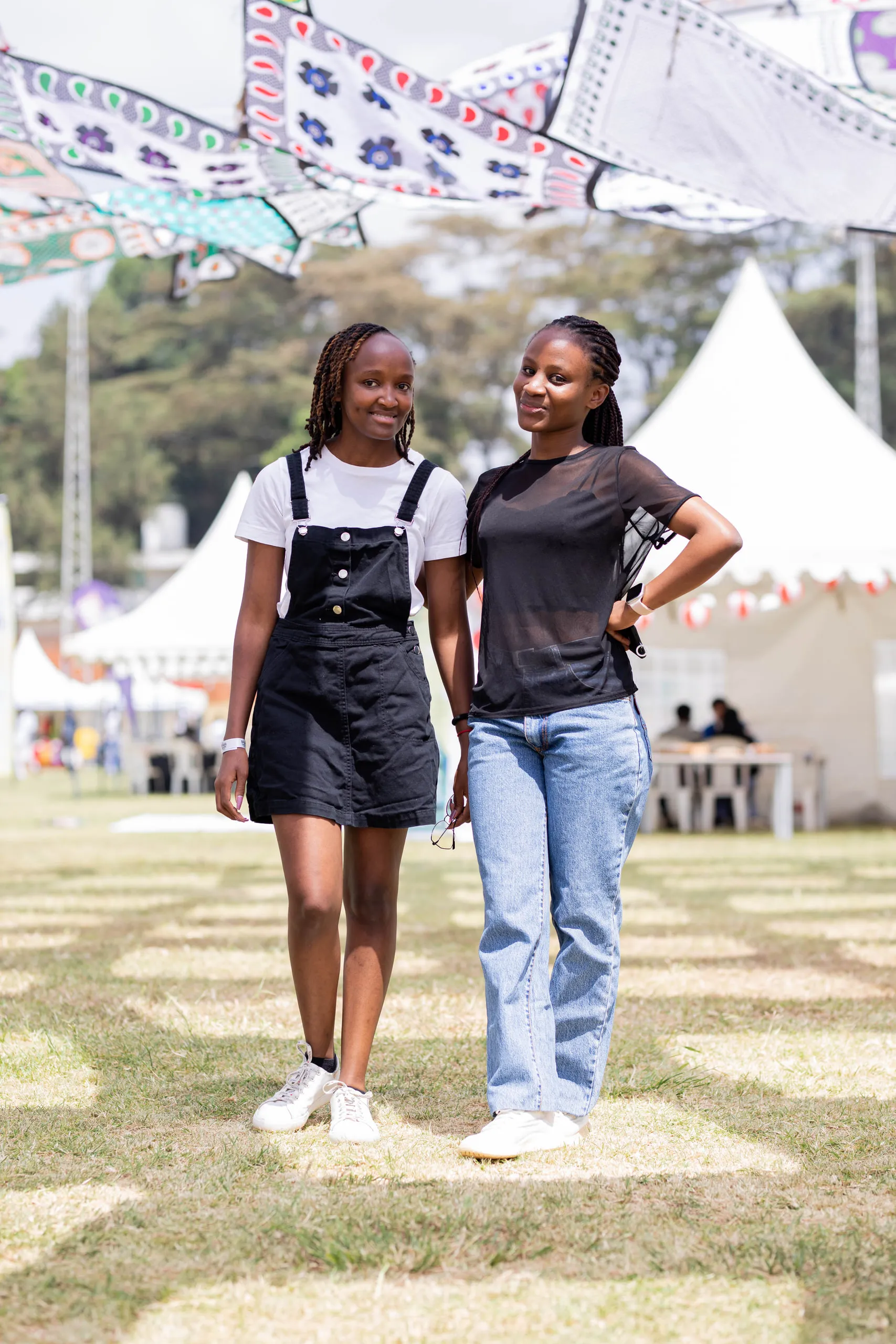 Two young women standing on the festival grounds under hanging patterned kites