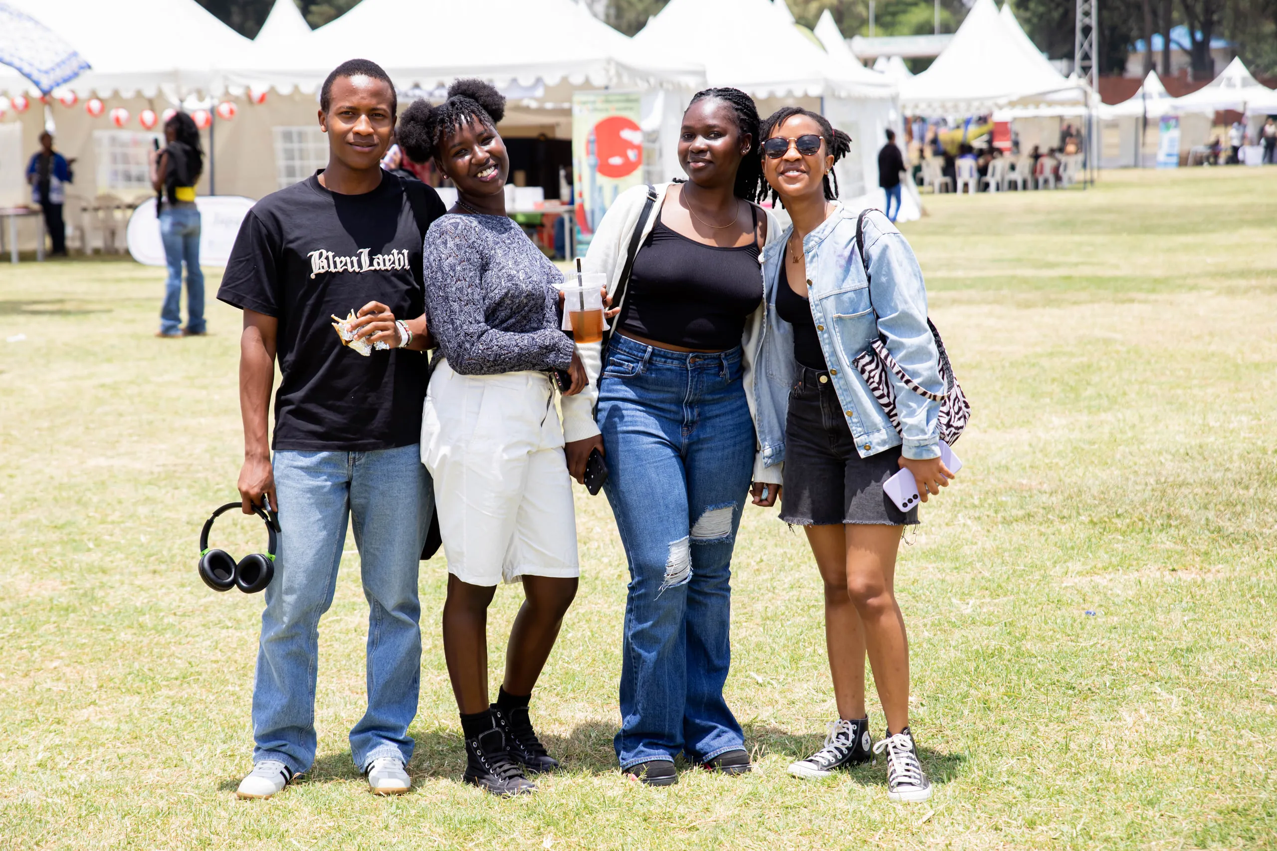 Four friends posing together on the lawn in front of white festival tents