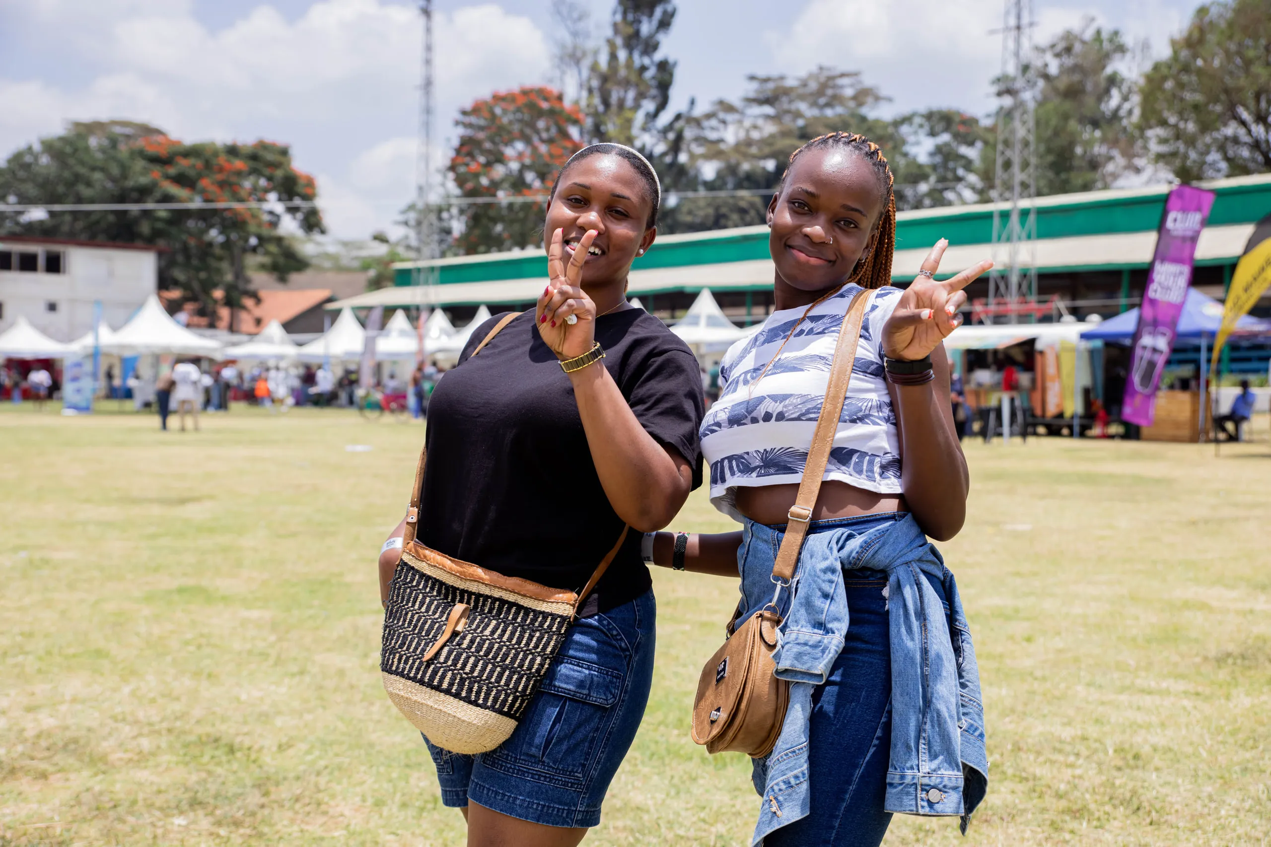 Two women flashing peace signs on the grass at an outdoor festival