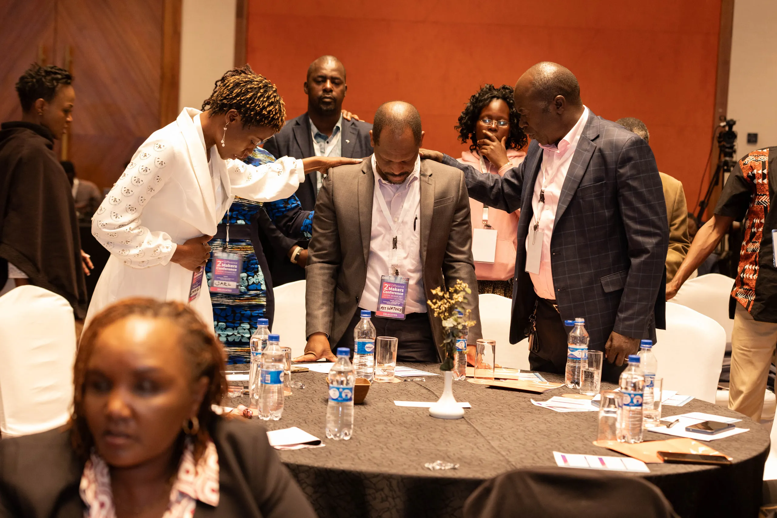 Colleagues standing around a conference table with hands on a man's shoulders in prayer