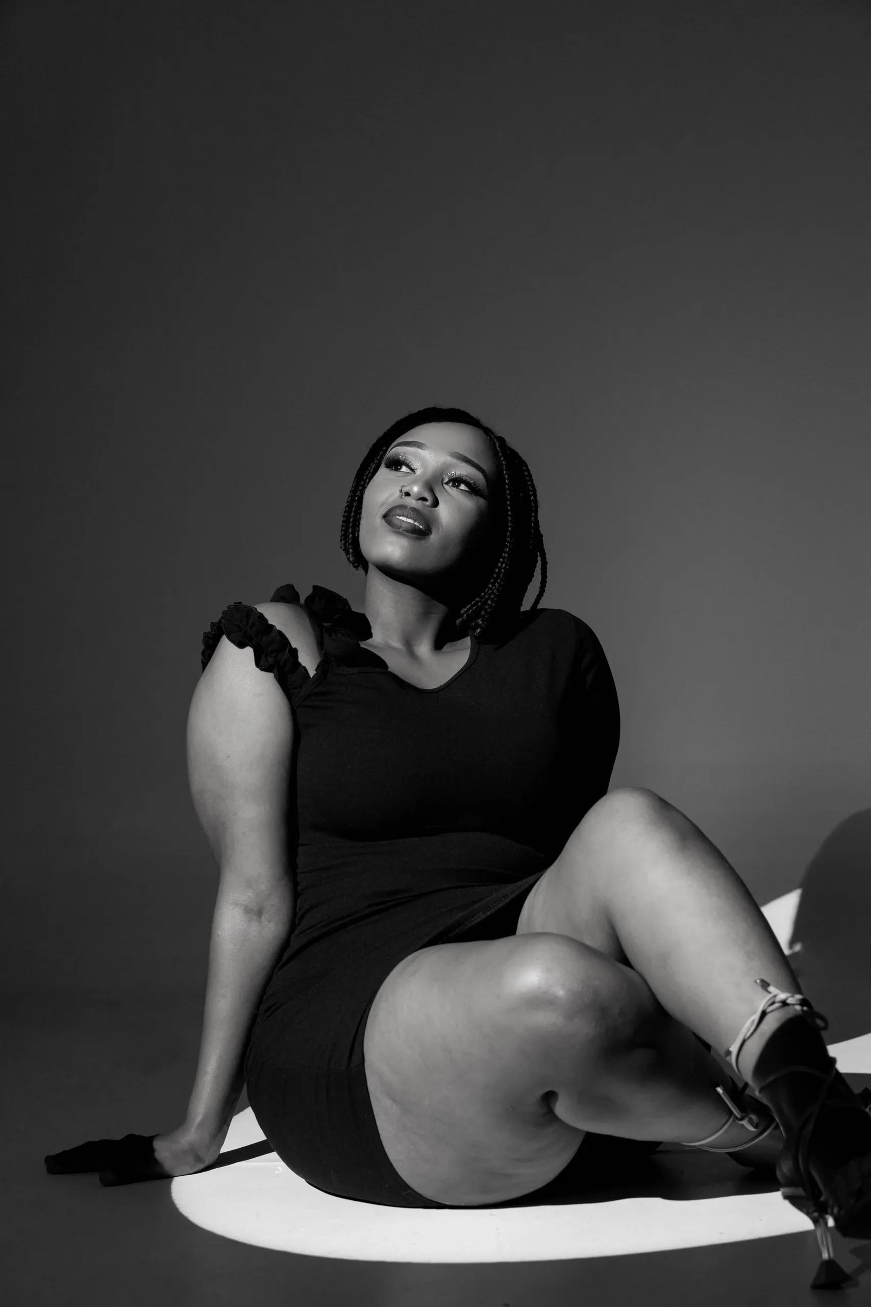 Woman in a black dress sitting in a spotlight and looking up, in black and white