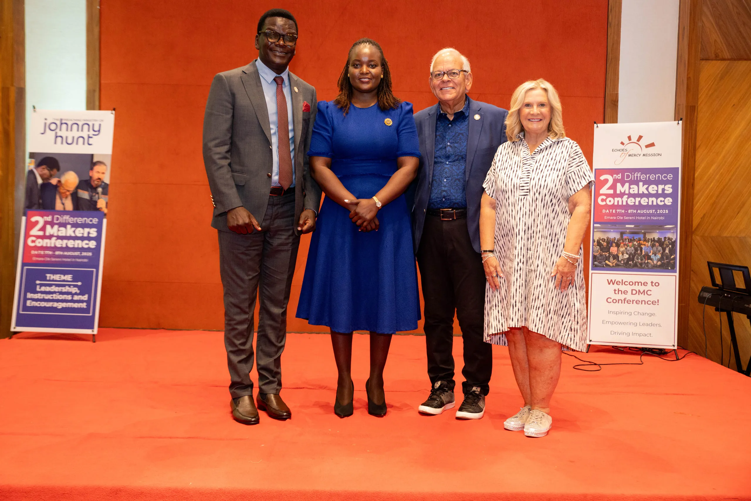 Four people posing in front of two conference banners on a red stage