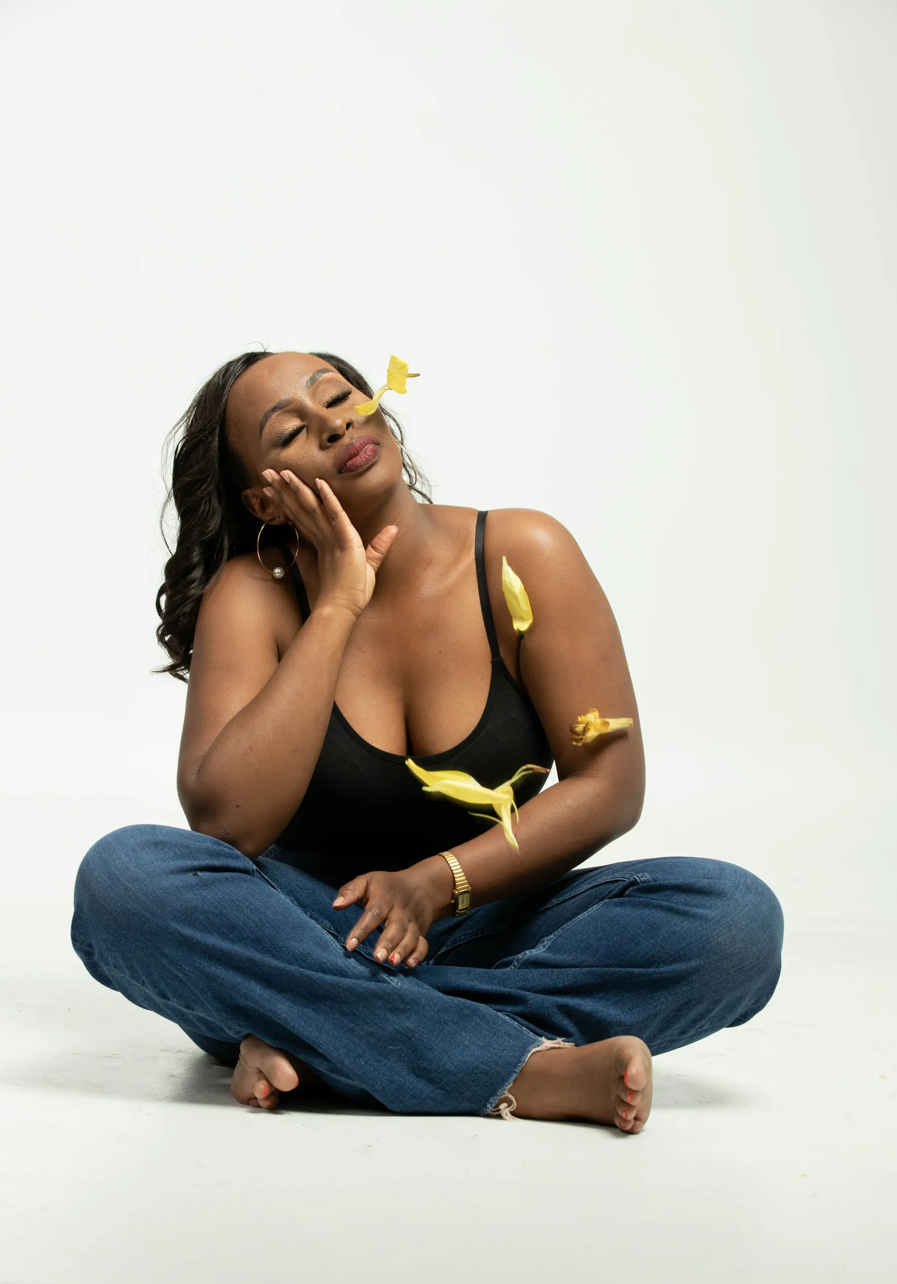 Woman in jeans sitting cross-legged on the floor with yellow petals falling around her