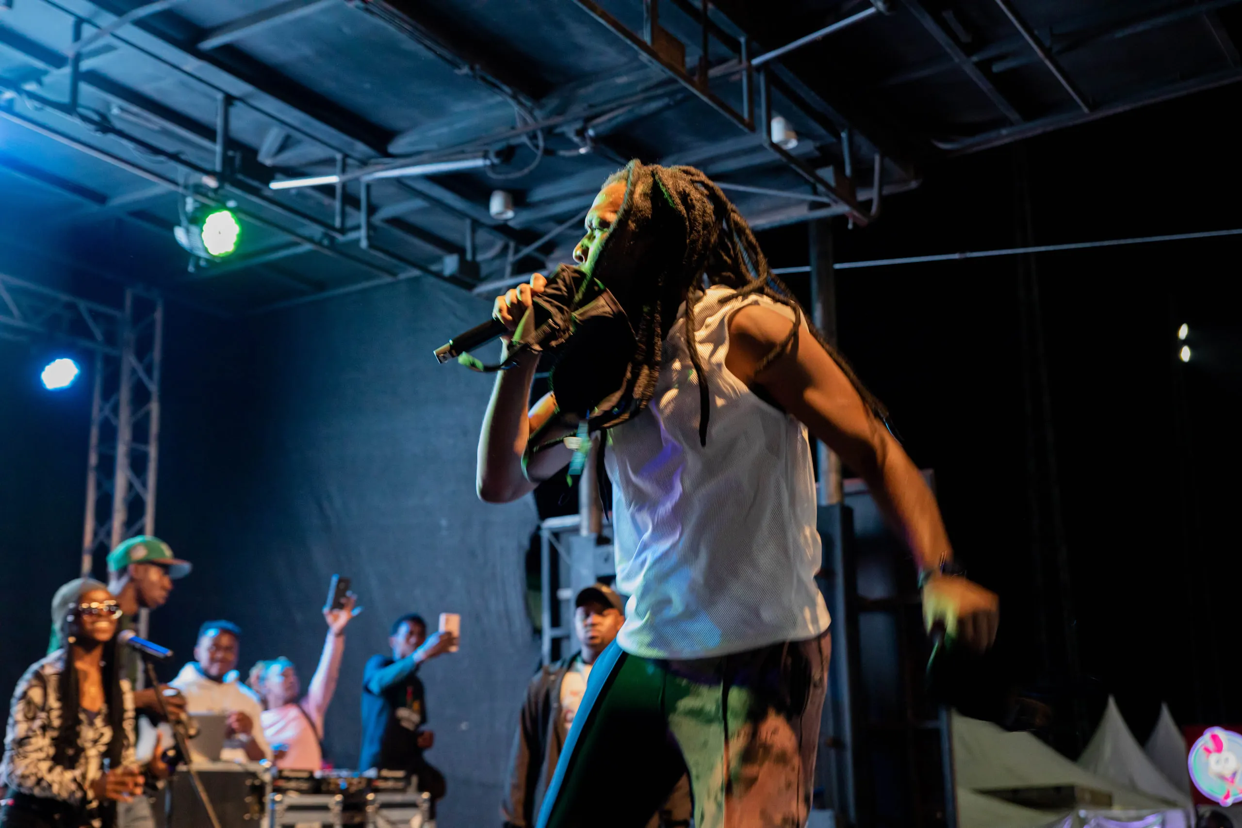 Performer in a white vest rapping into a microphone under stage lights