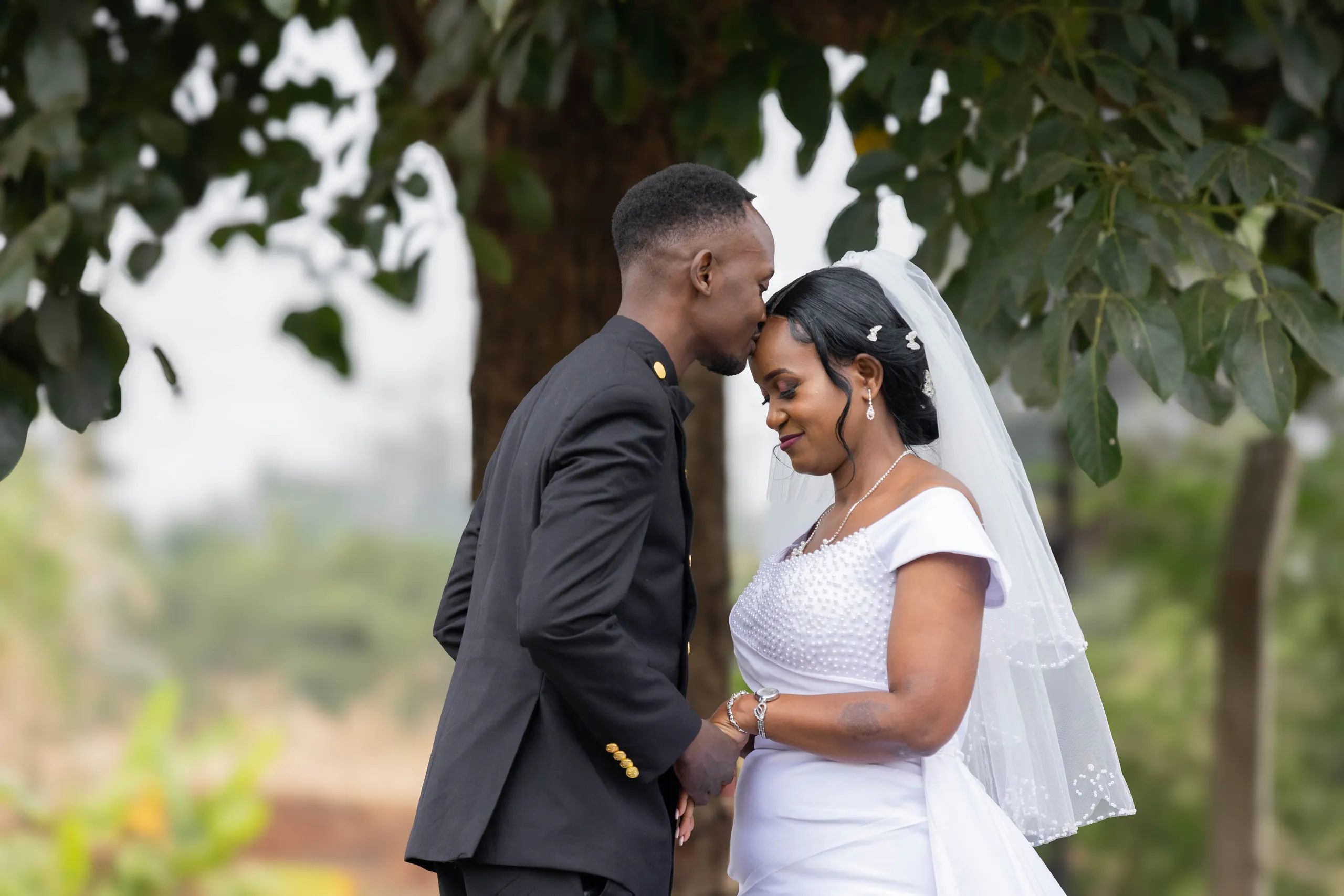 Groom kissing the bride's forehead under a tree
