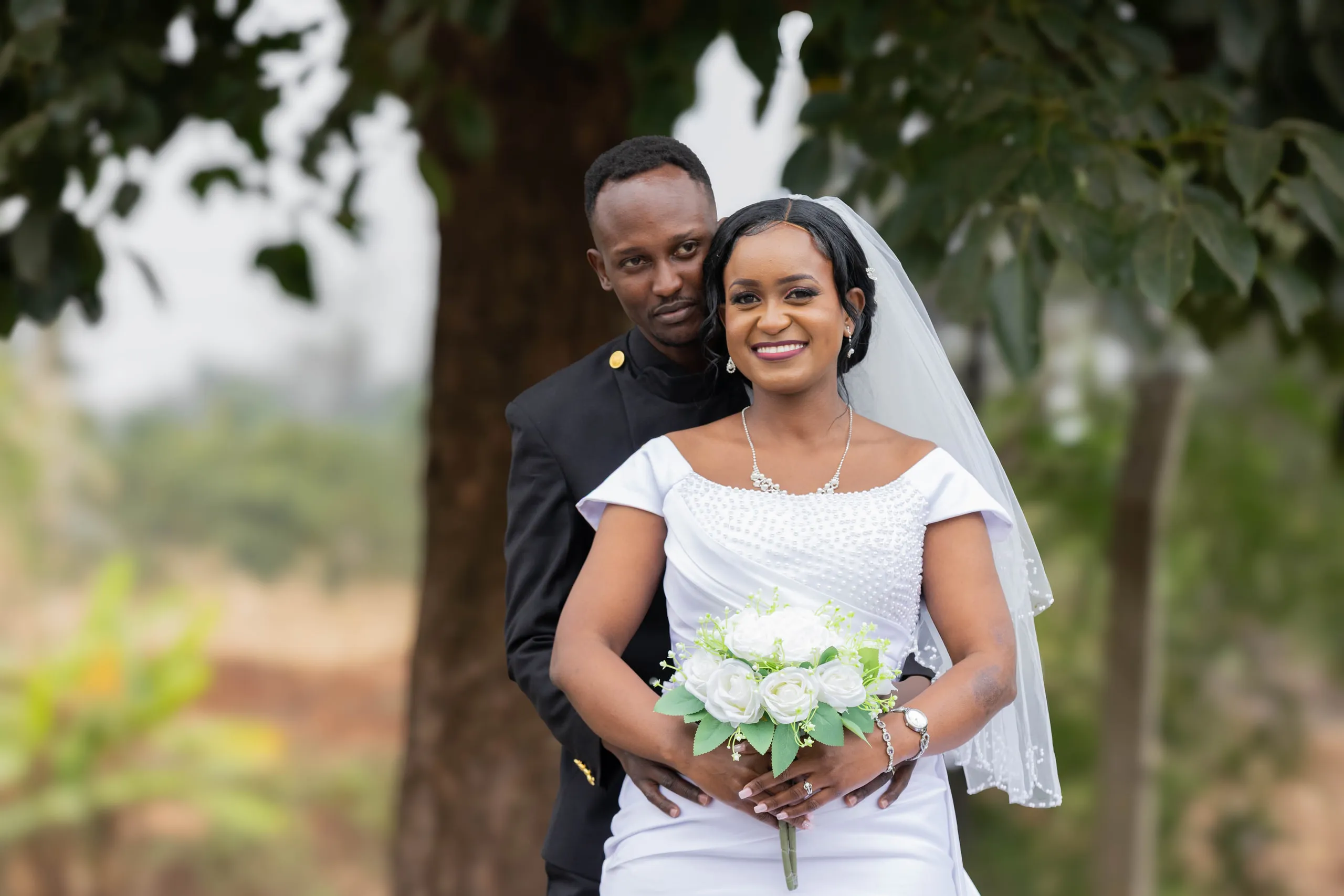 Smiling bride holding her bouquet with the groom behind her
