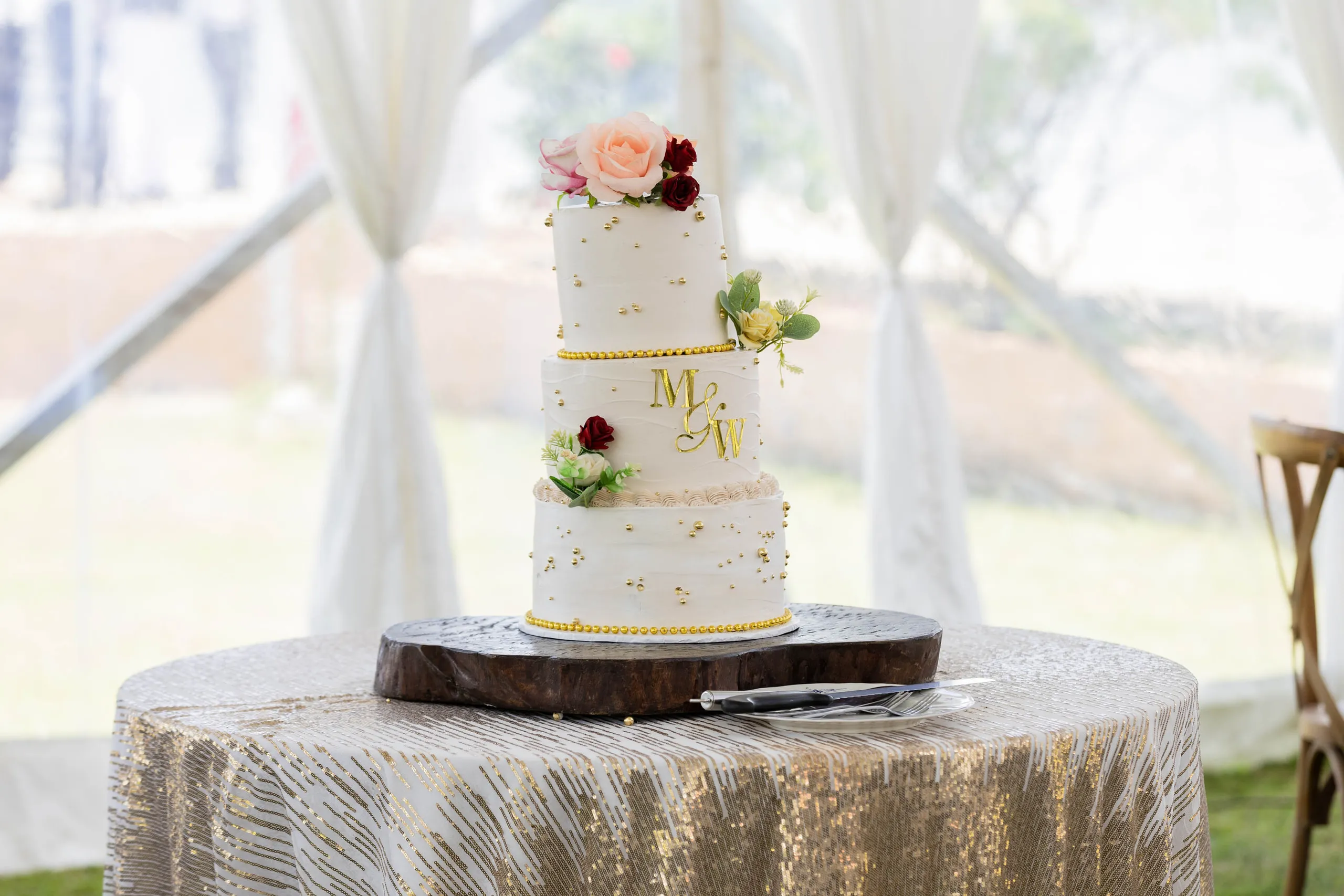 Three-tier white cake with flowers on a gold table under a tent