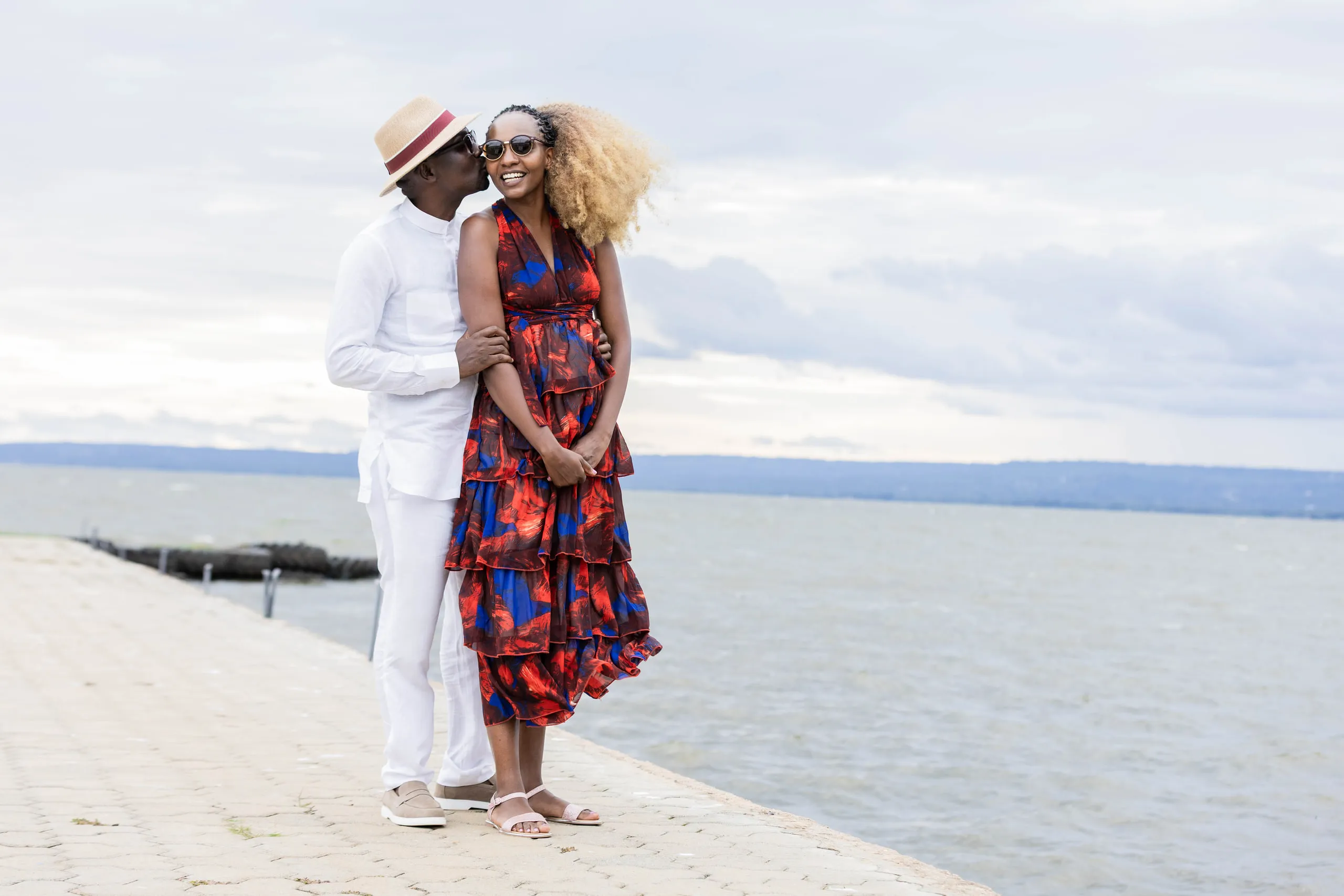 Couple on a lakeside jetty, she in red and blue, he in white with a hat