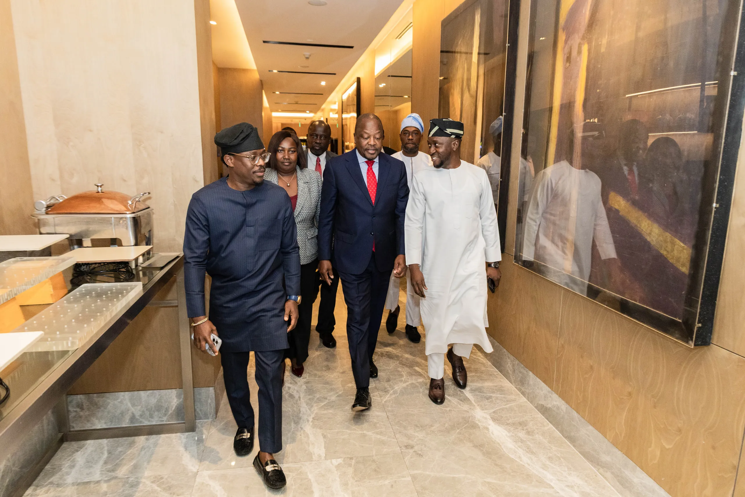 Group of men in suits and traditional dress walking along a marble hotel corridor