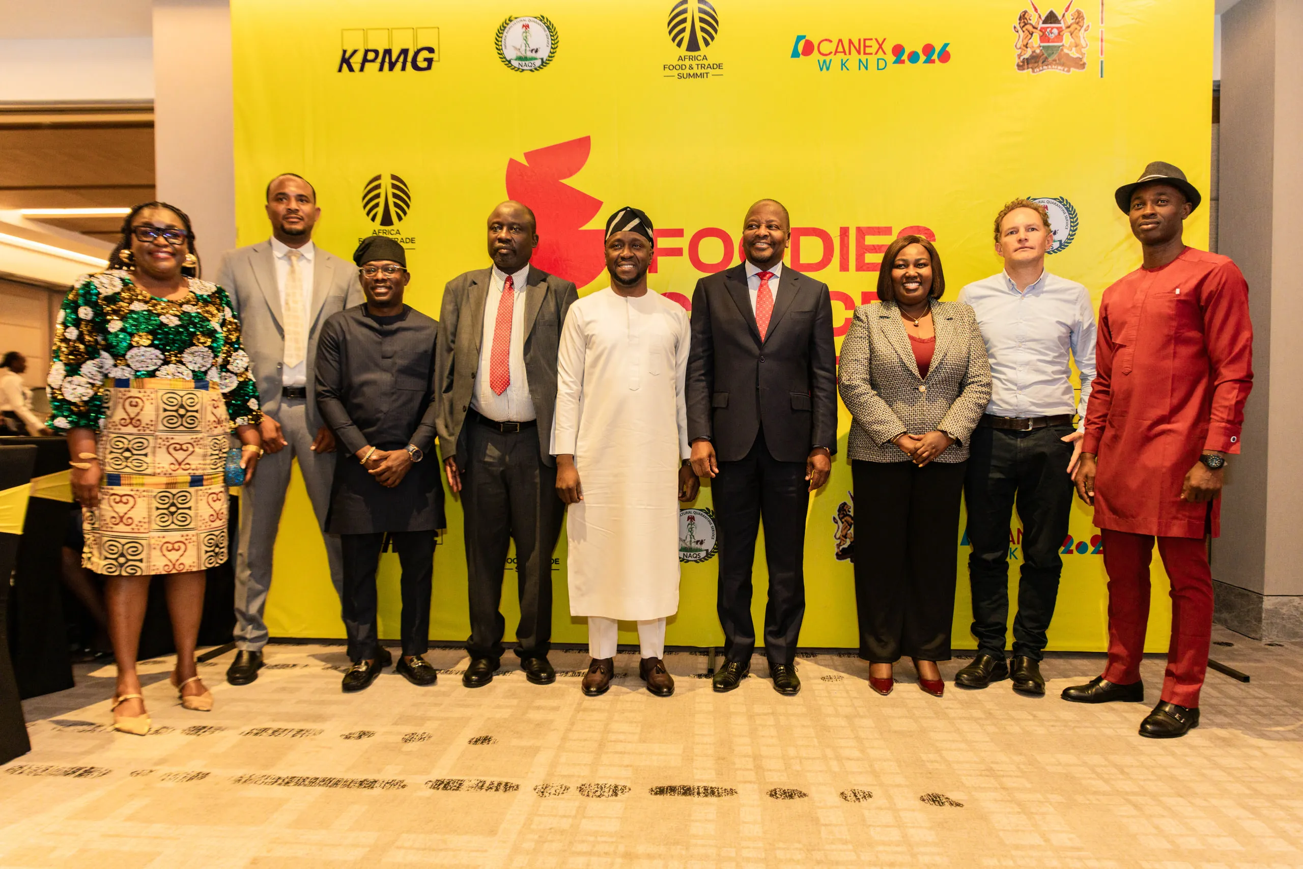 Eleven guests in suits and traditional dress posing in front of a yellow event backdrop