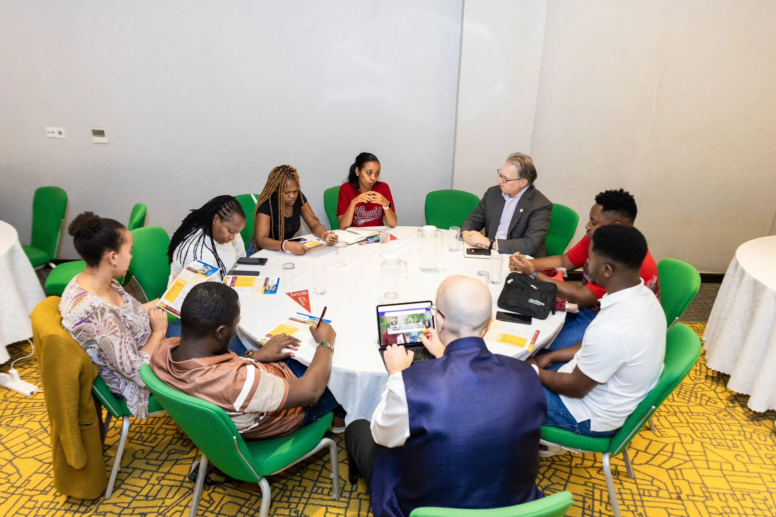Eight people seated around a white round table with brochures and a tablet