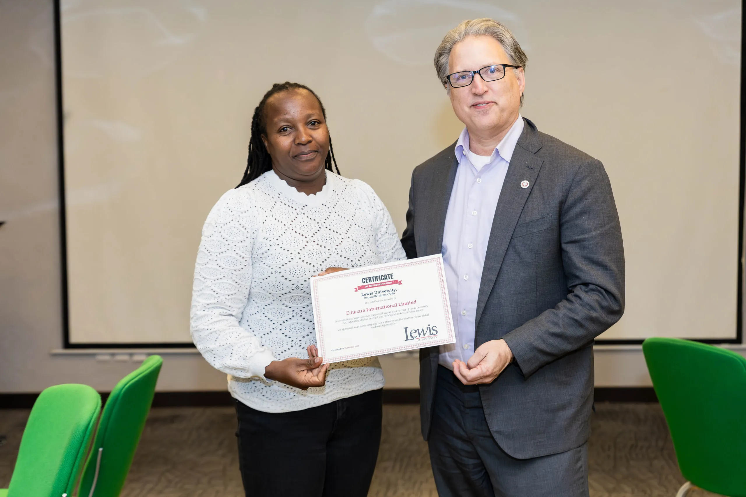 Man in a grey blazer handing a framed certificate to a woman in a white lace top
