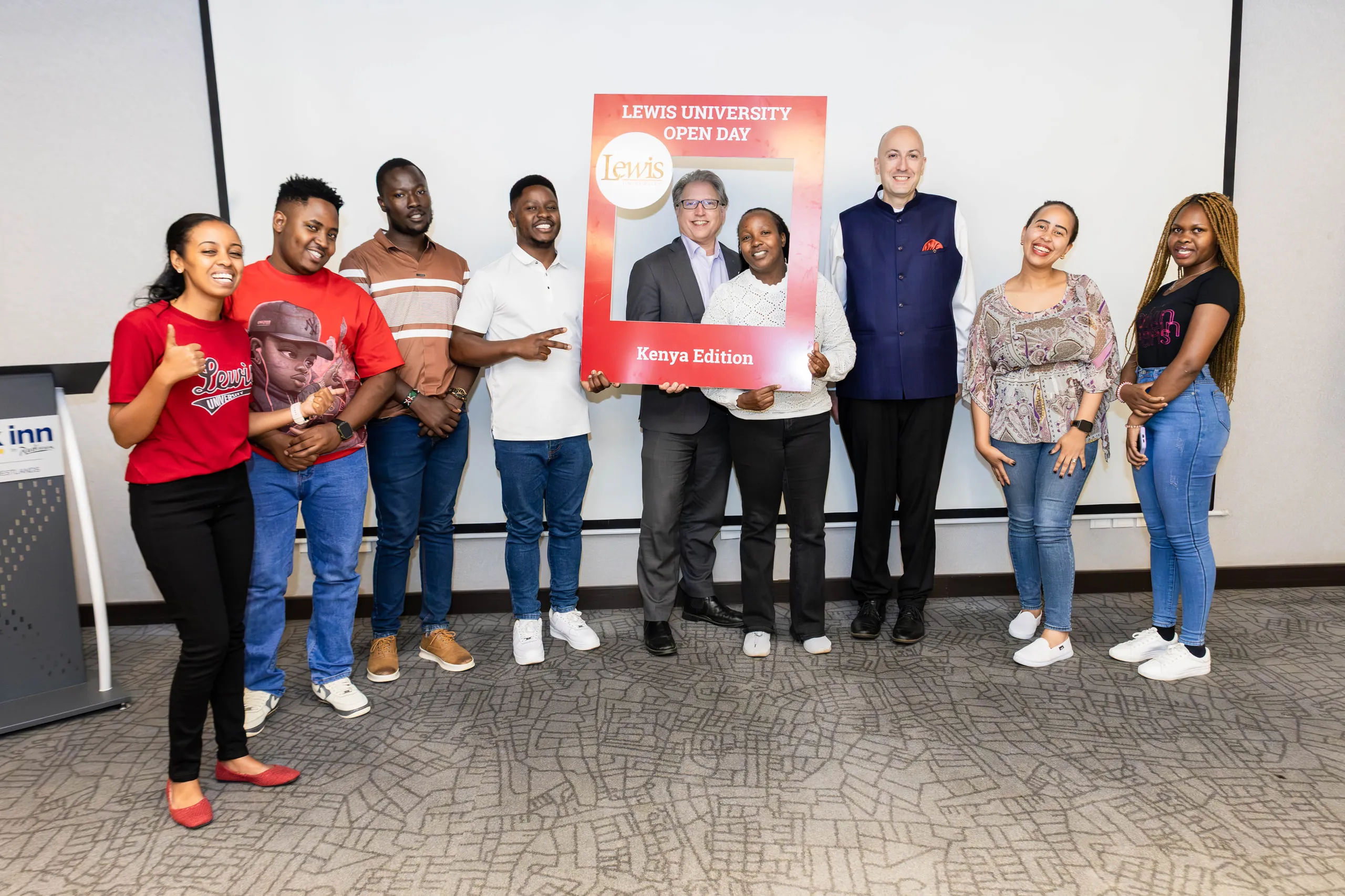 Eight people and two guests holding a red photo frame in front of a white screen