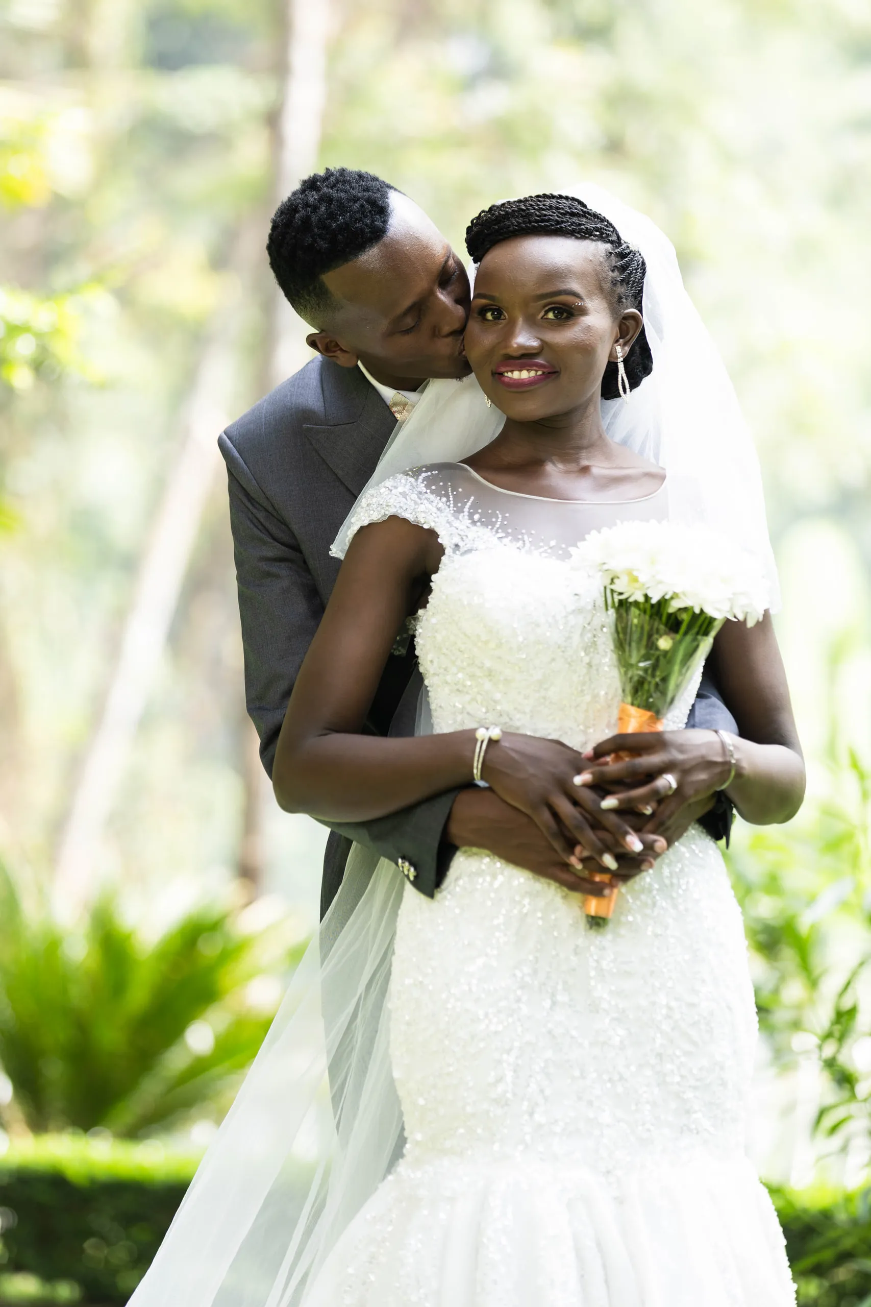 Groom kissing the bride's cheek from behind as she holds her bouquet