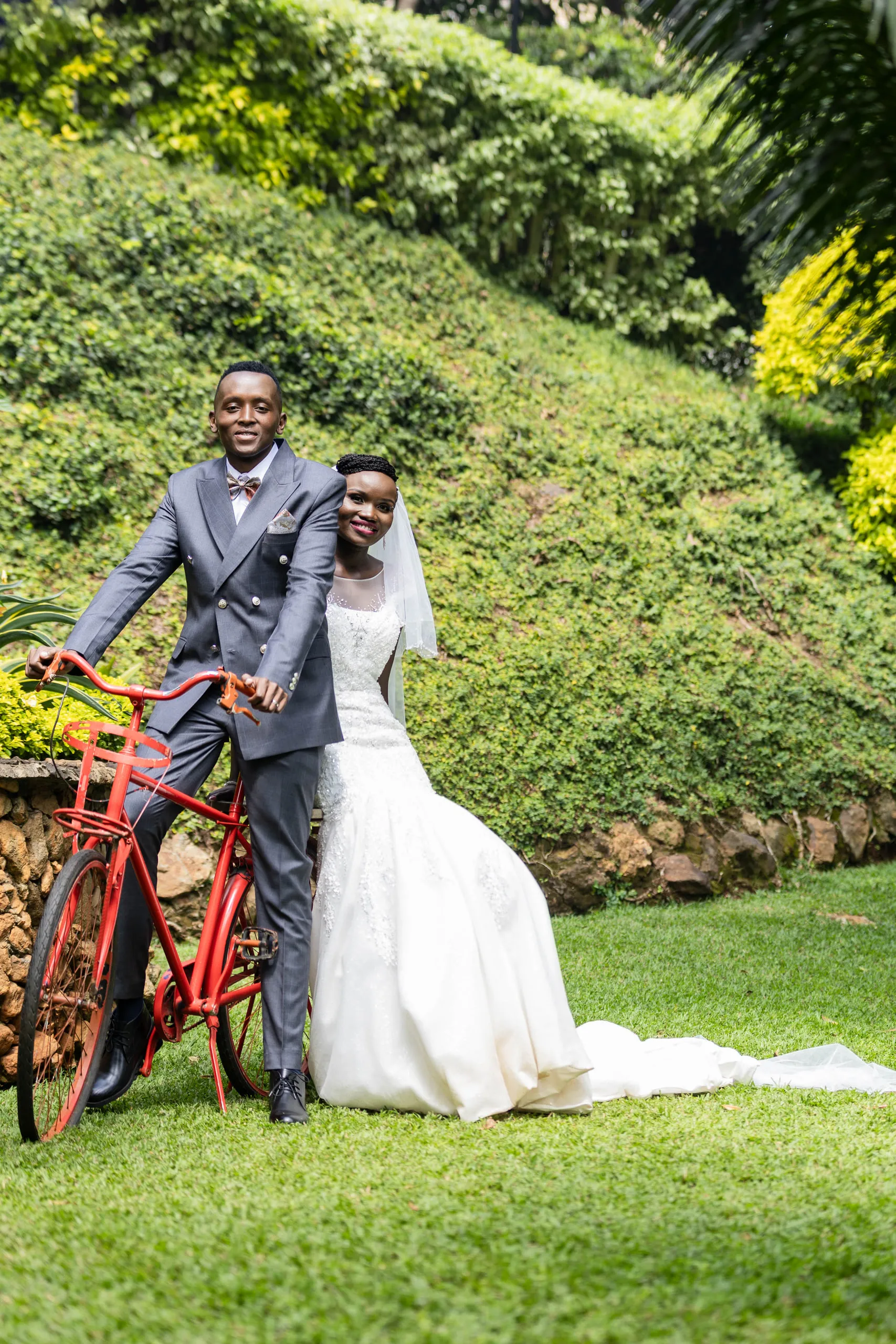 Groom sitting on a red bicycle with the bride beside him