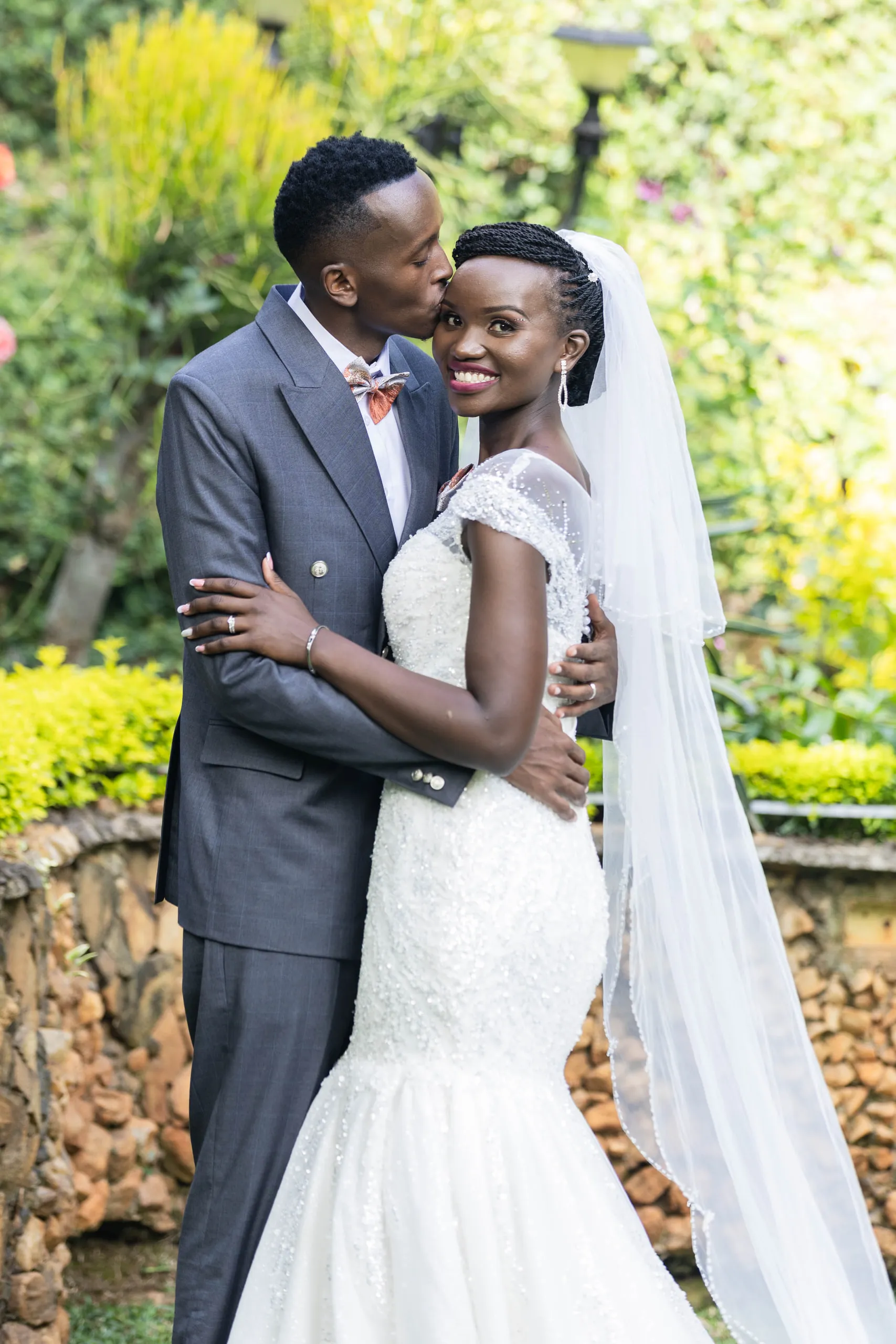 Groom kissing the bride beside a stone wall in the garden