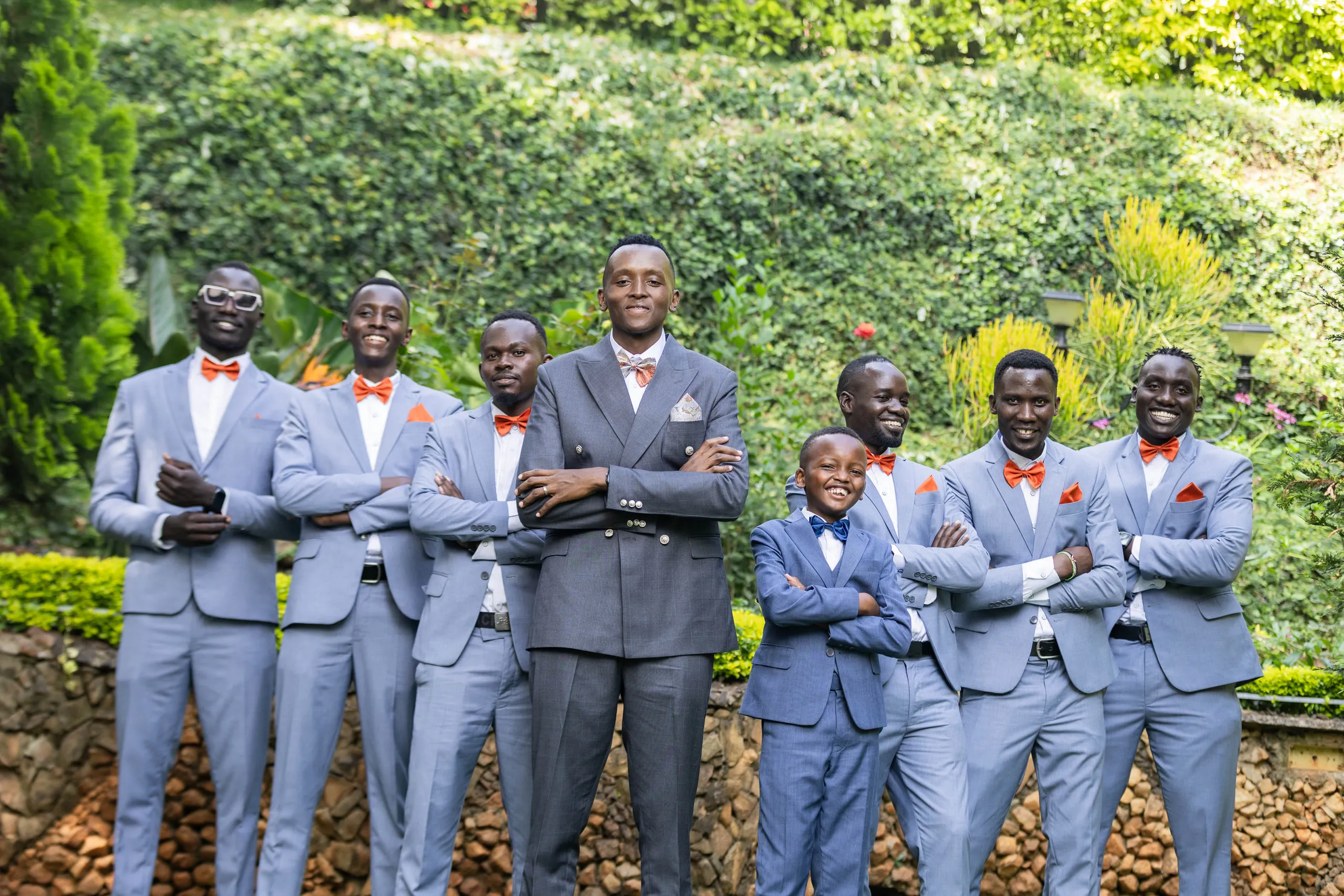 Groomsmen in blue suits standing in a line below a green hillside
